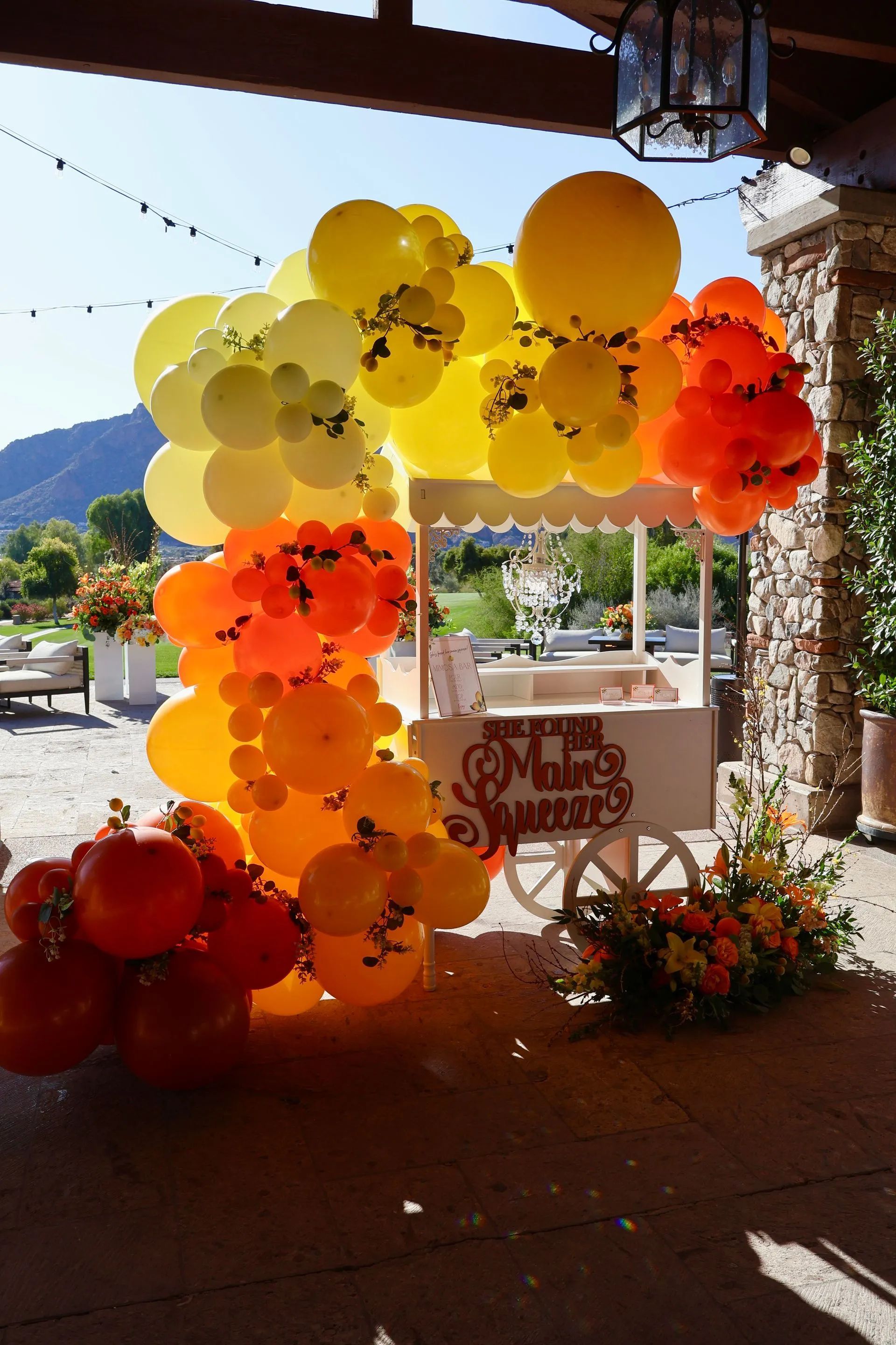 Yellow, orange, and red balloon arch at an outdoor event with mountains in the background.