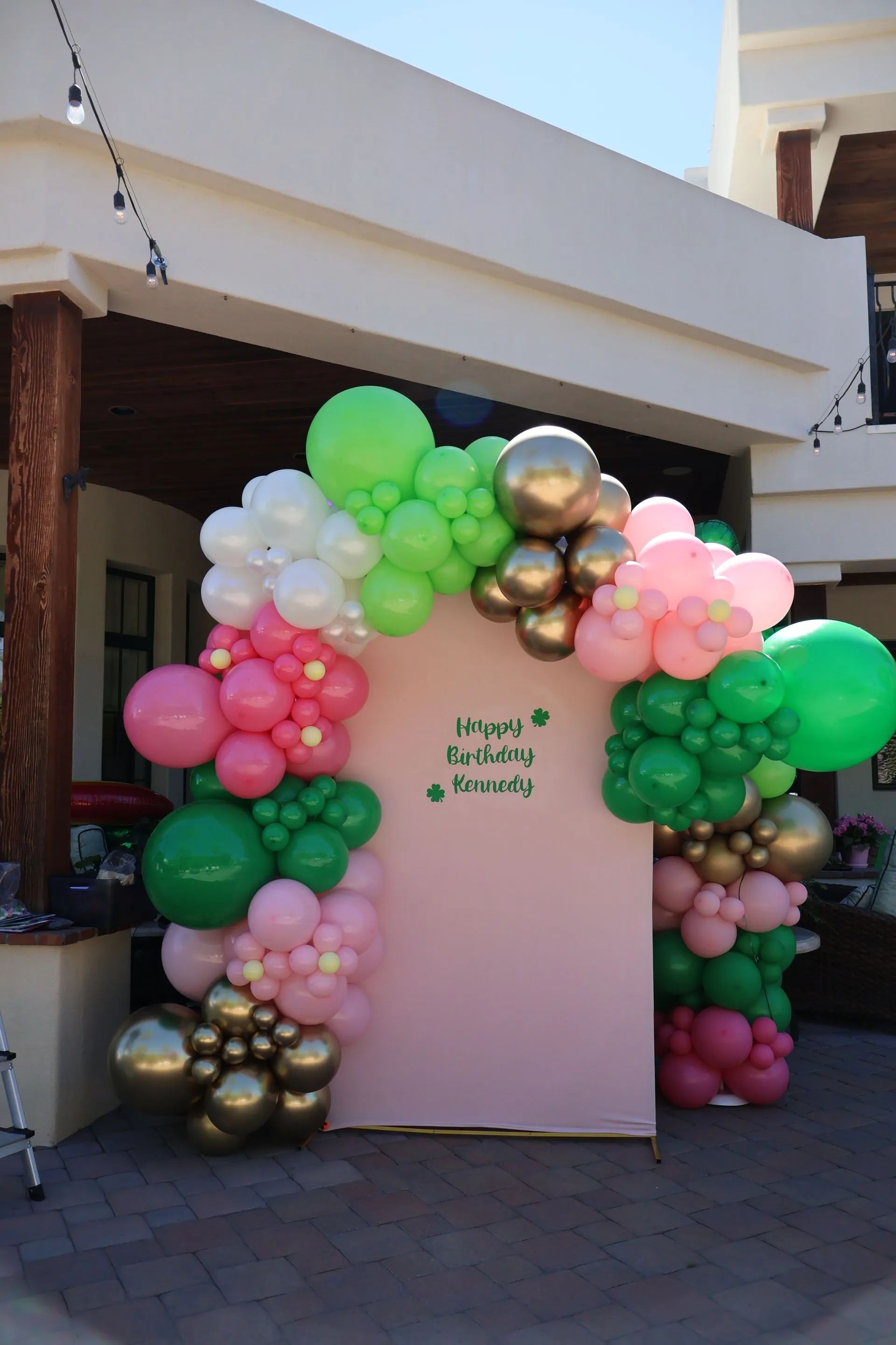 Pink photo backdrop framed by pastel balloons and gold accents outdoors