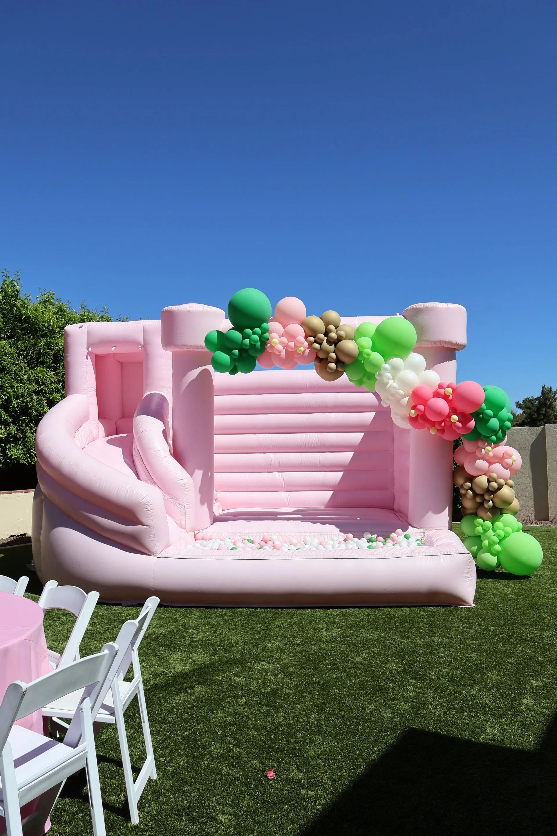 Pink inflatable bounce house with balloon decorations on a grassy lawn under a clear blue sky