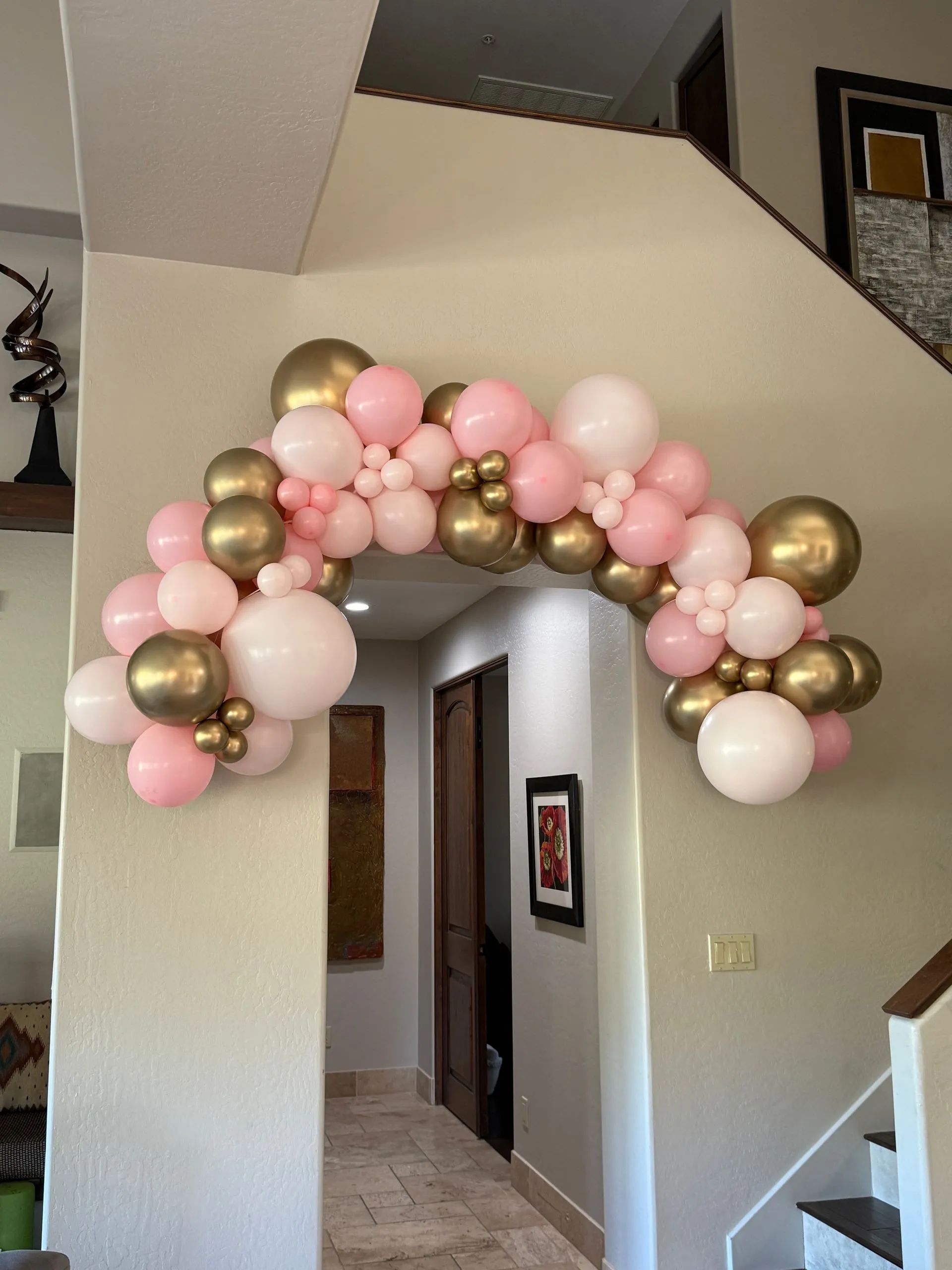 Pink, white, and gold balloon arch over an interior doorway in a home