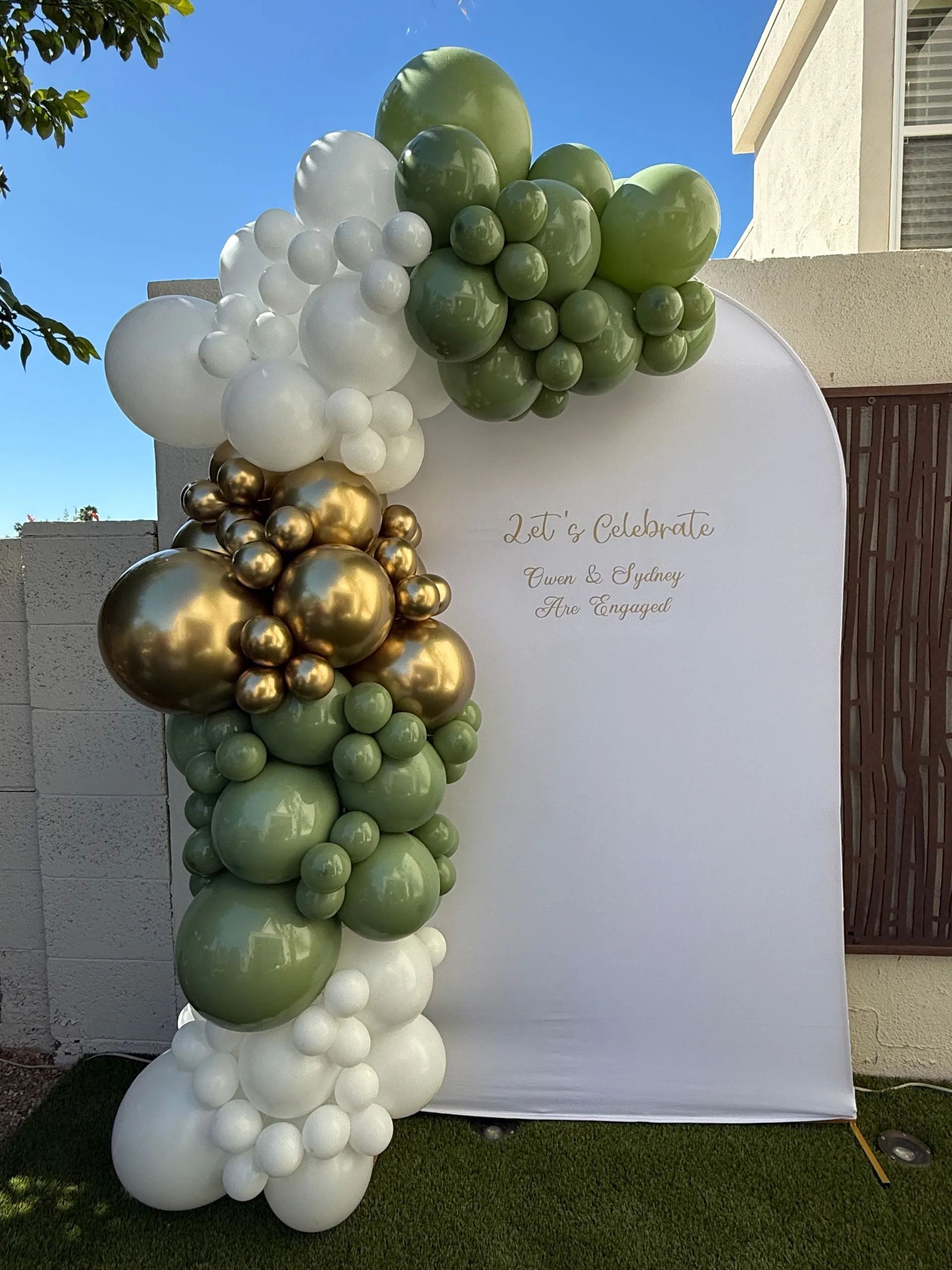 White, gold, and green balloon garland framing a white backdrop at an outdoor event