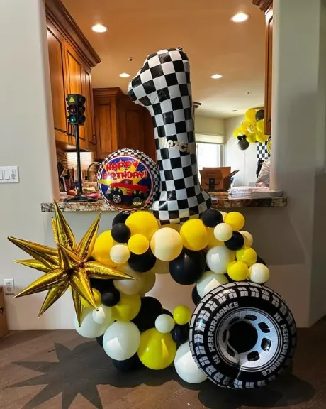 Racing-themed balloon display with black, white, and yellow balloons, checkered pattern, and star decoration