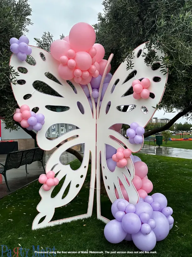 White butterfly balloon sculpture with pink and purple balloon flowers in an outdoor park setting