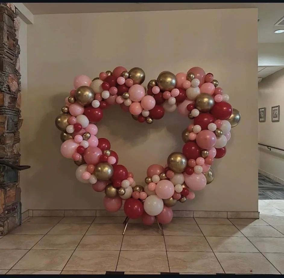 Heart-shaped balloon arrangement in pink, white, and gold against an indoor wall