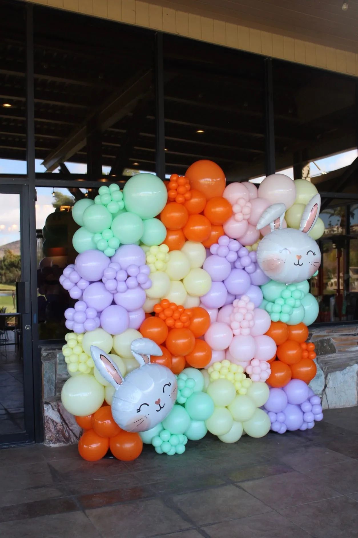 Pastel balloon wall with bunny-face balloons displayed outdoors under a covered walkway
