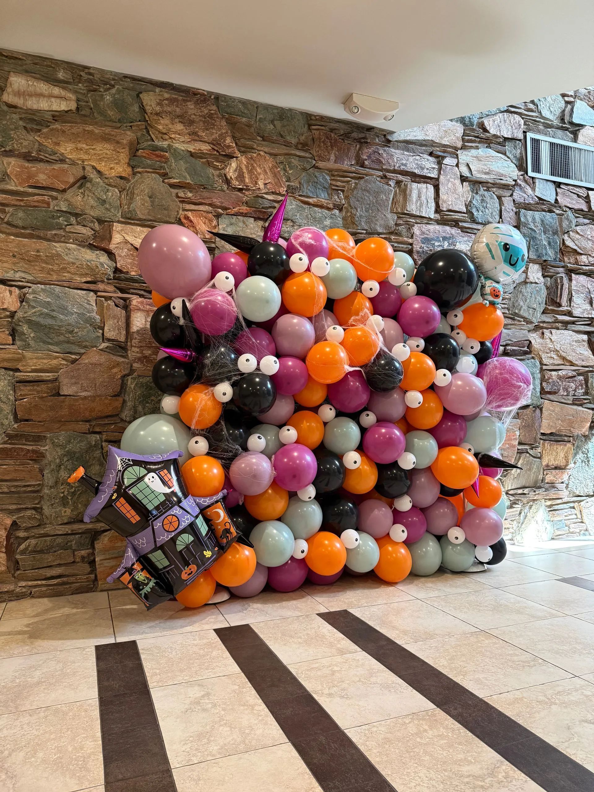 Colorful balloon arch installation against a stone wall in an indoor lobby