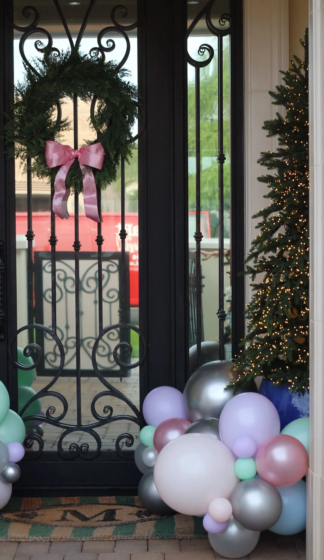 Decorated front porch with wreath, pink bow, Christmas lights, and pastel balloon clusters