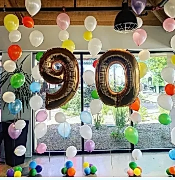 Gold balloon “90” birthday display with colorful balloons in a decorated room
