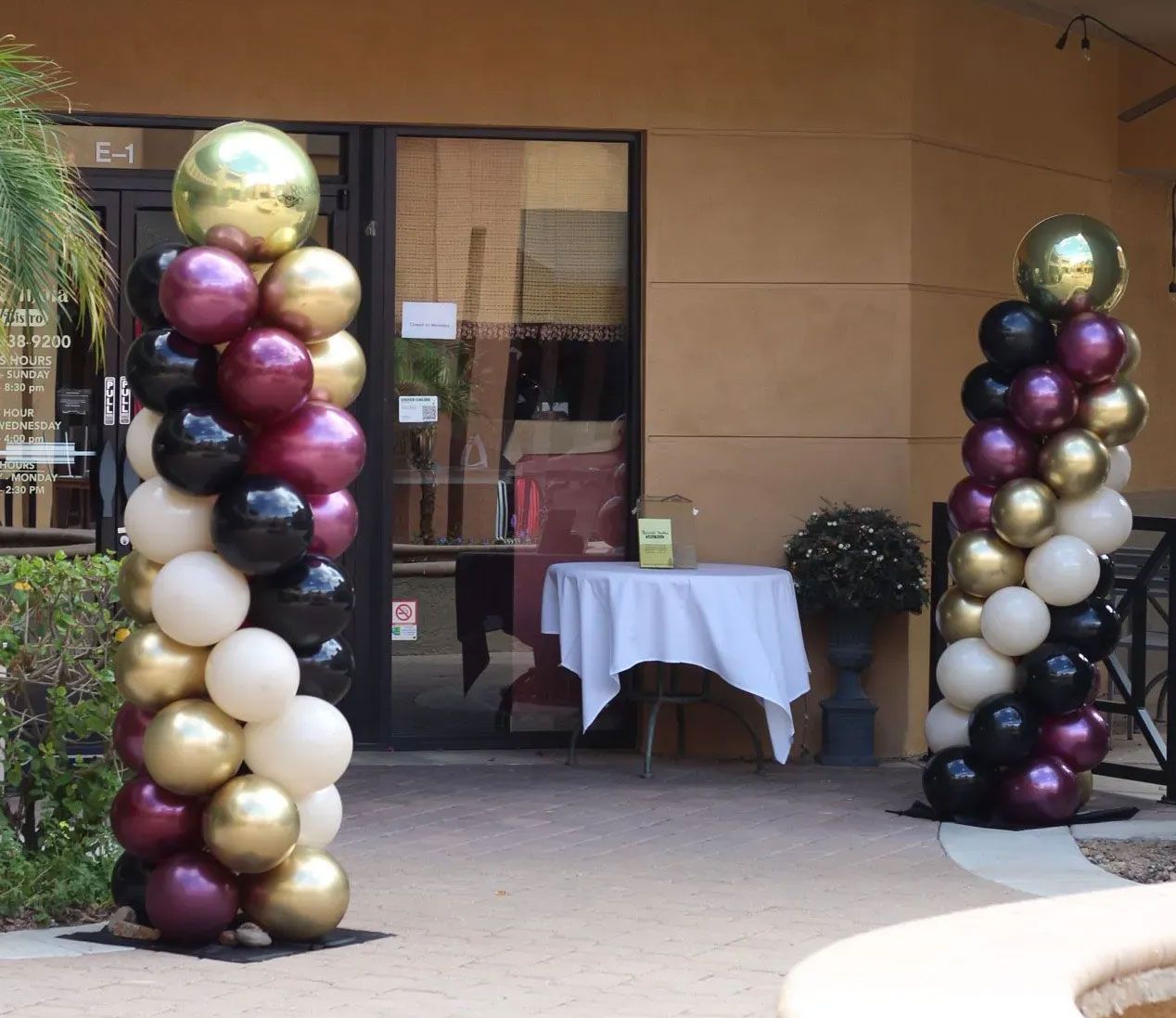Balloon columns in black, gold, white, and burgundy beside a building entrance outdoors