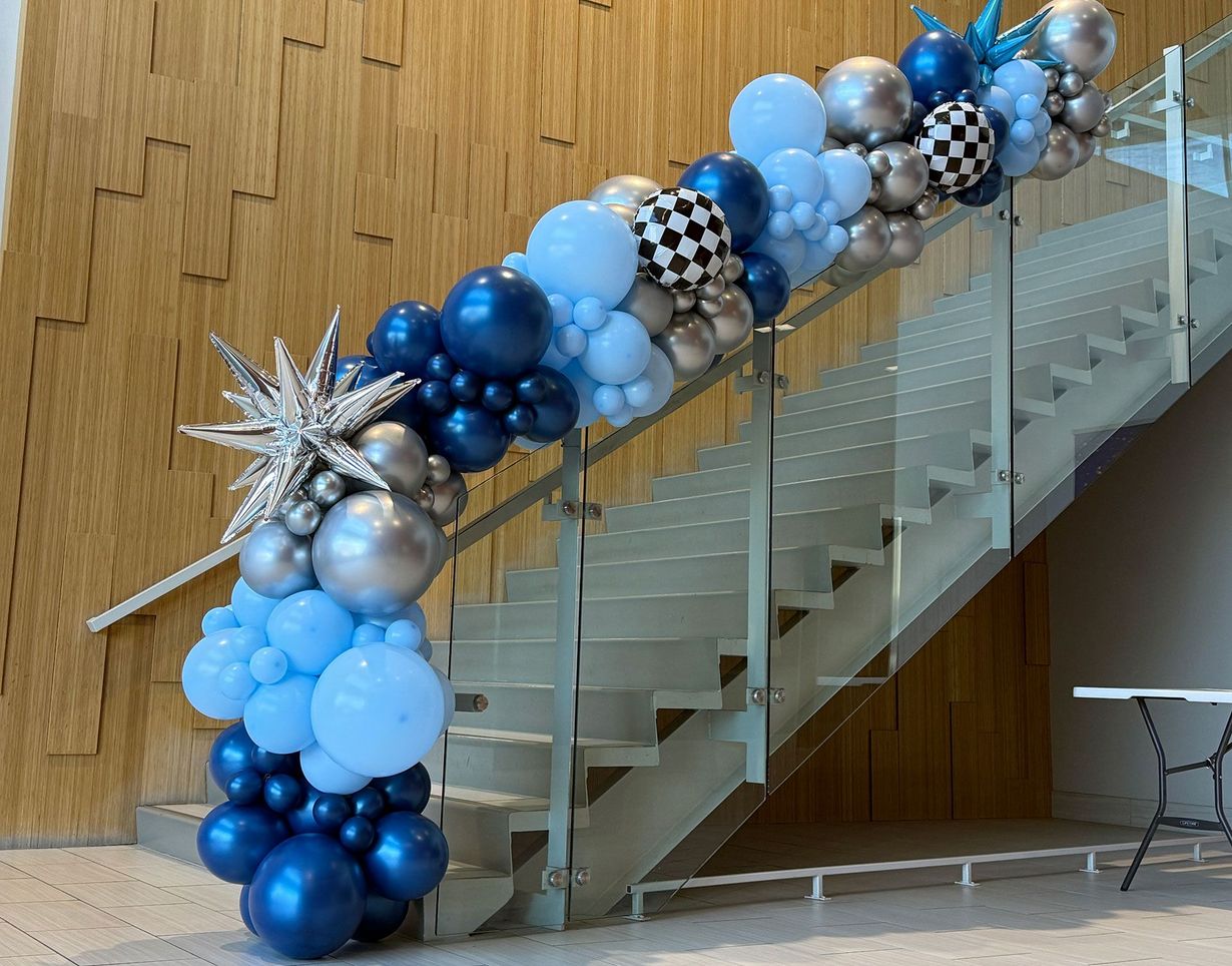 Blue, silver, and black balloon garland arched along a staircase in a modern lobby