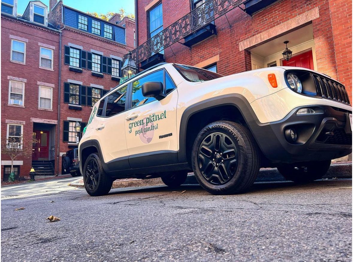 A white jeep renegade is parked in front of a brick building.
