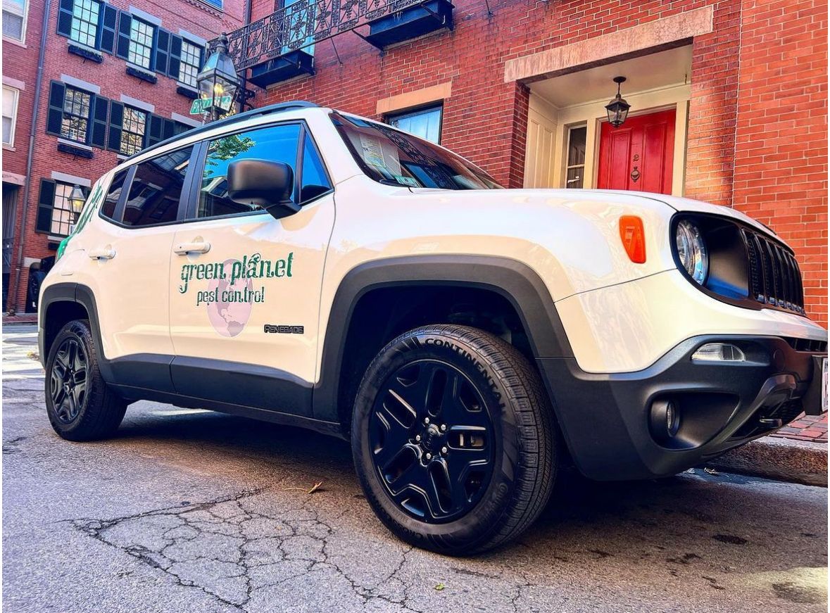 A white jeep renegade is parked in front of a brick building.