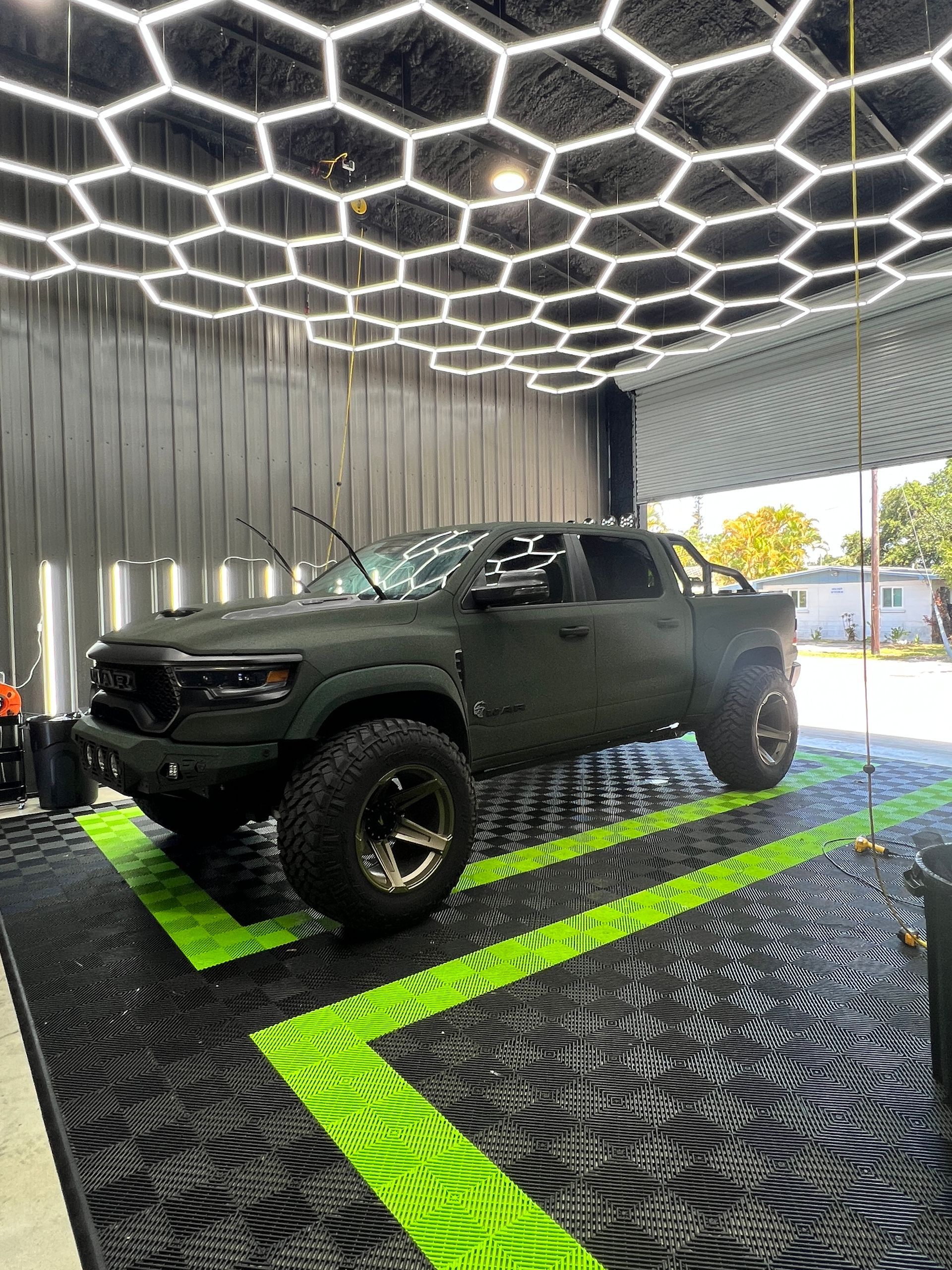 A black truck is parked in a garage with a honeycomb ceiling.