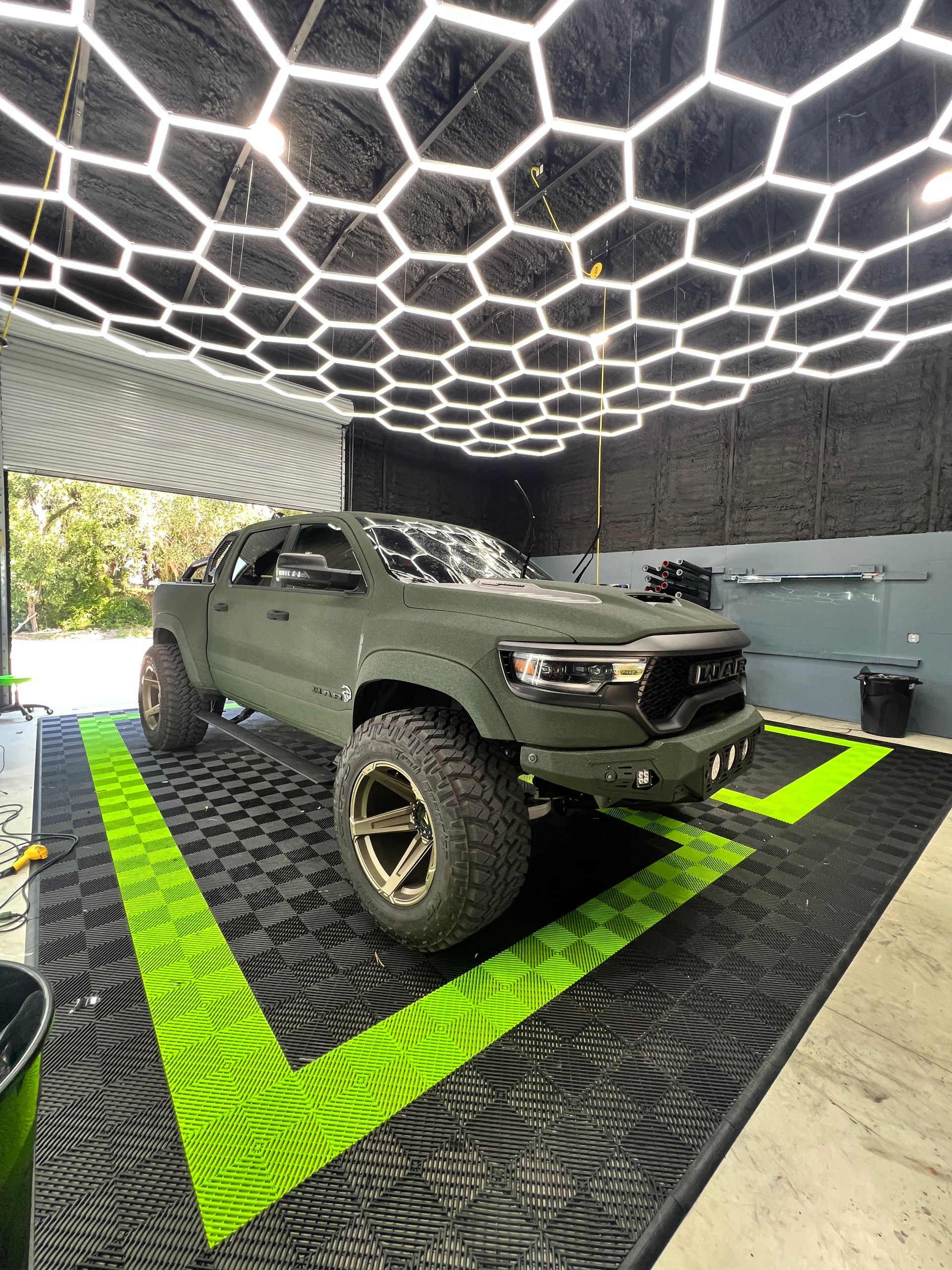 A green truck is parked in a garage with a honeycomb ceiling.