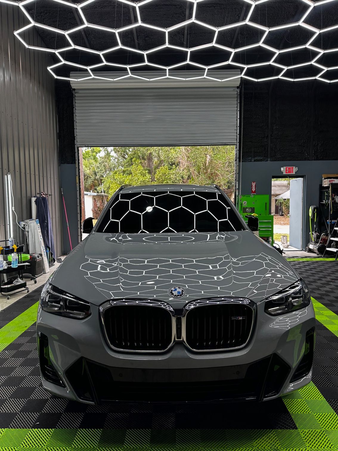 A bmw x3 is parked in a garage under a honeycomb ceiling.