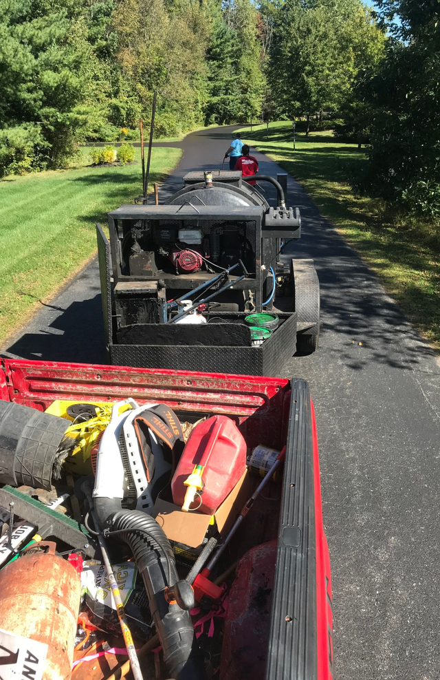 Red pickup truck towing a black trailer with equipment on a paved driveway in a yard.