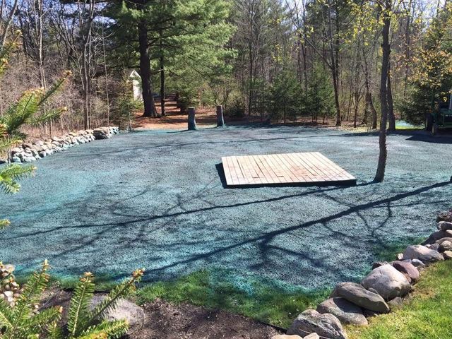 Newly seeded yard with a wooden platform, surrounded by a rock border and trees in the background.