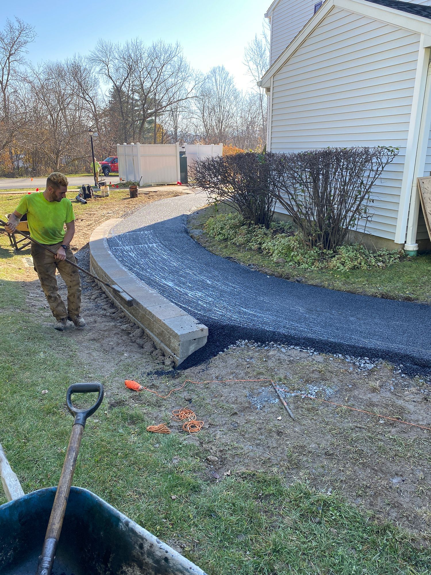 Man working on asphalt driveway, holding a level. Gray gravel border, house in the background.