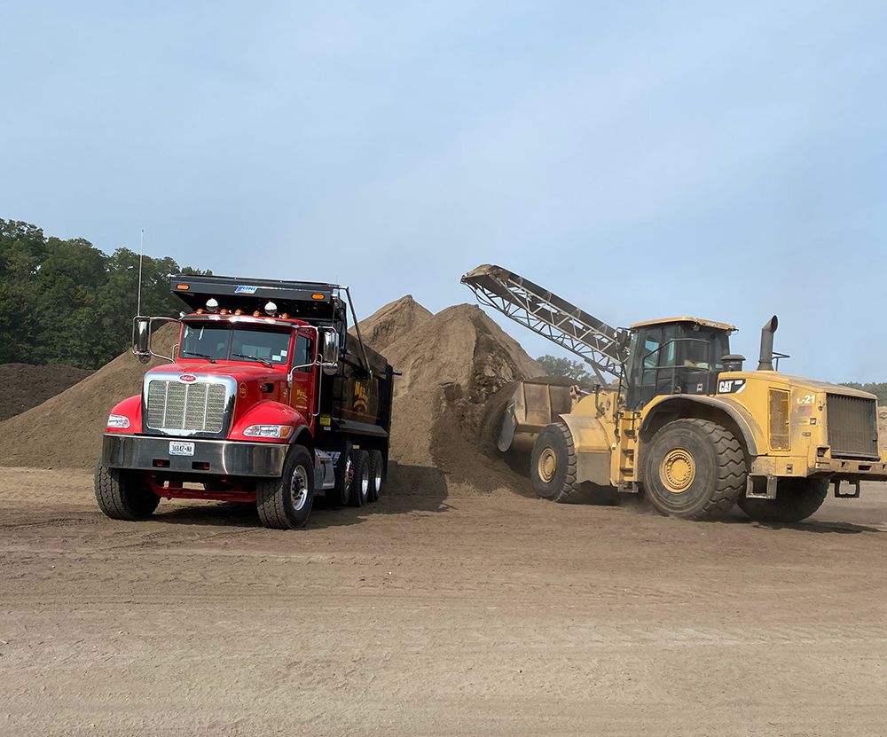 Red dump truck being loaded with material by a yellow loader in an outdoor yard.