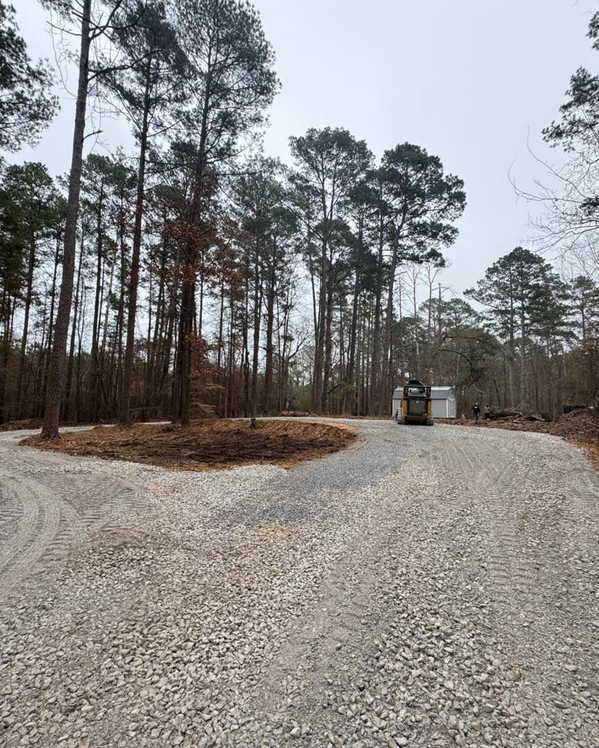 Gravel driveway leads to a small vehicle parked near trees and a clearing. Overcast day.