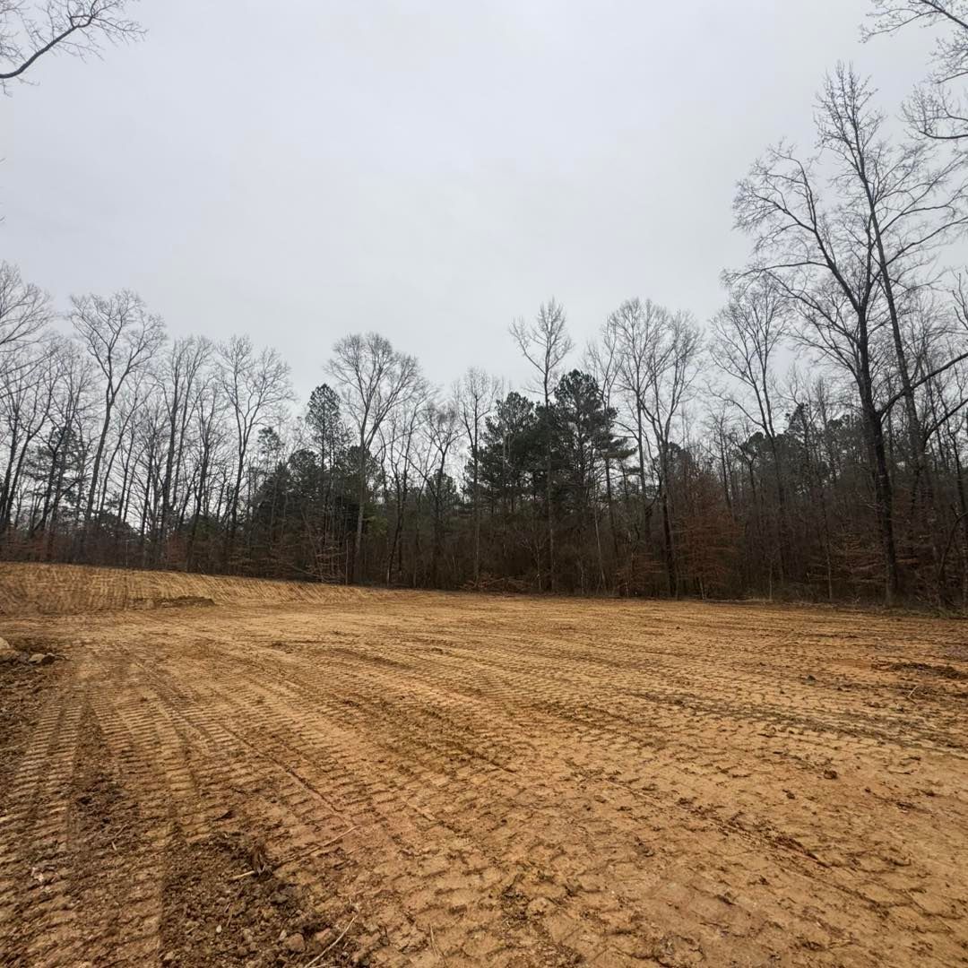 Cleared field with tire tracks, trees in the background, overcast sky.