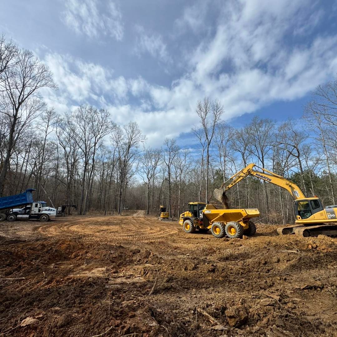 Construction site with heavy machinery, including dump trucks and excavators, clearing land under a cloudy sky.