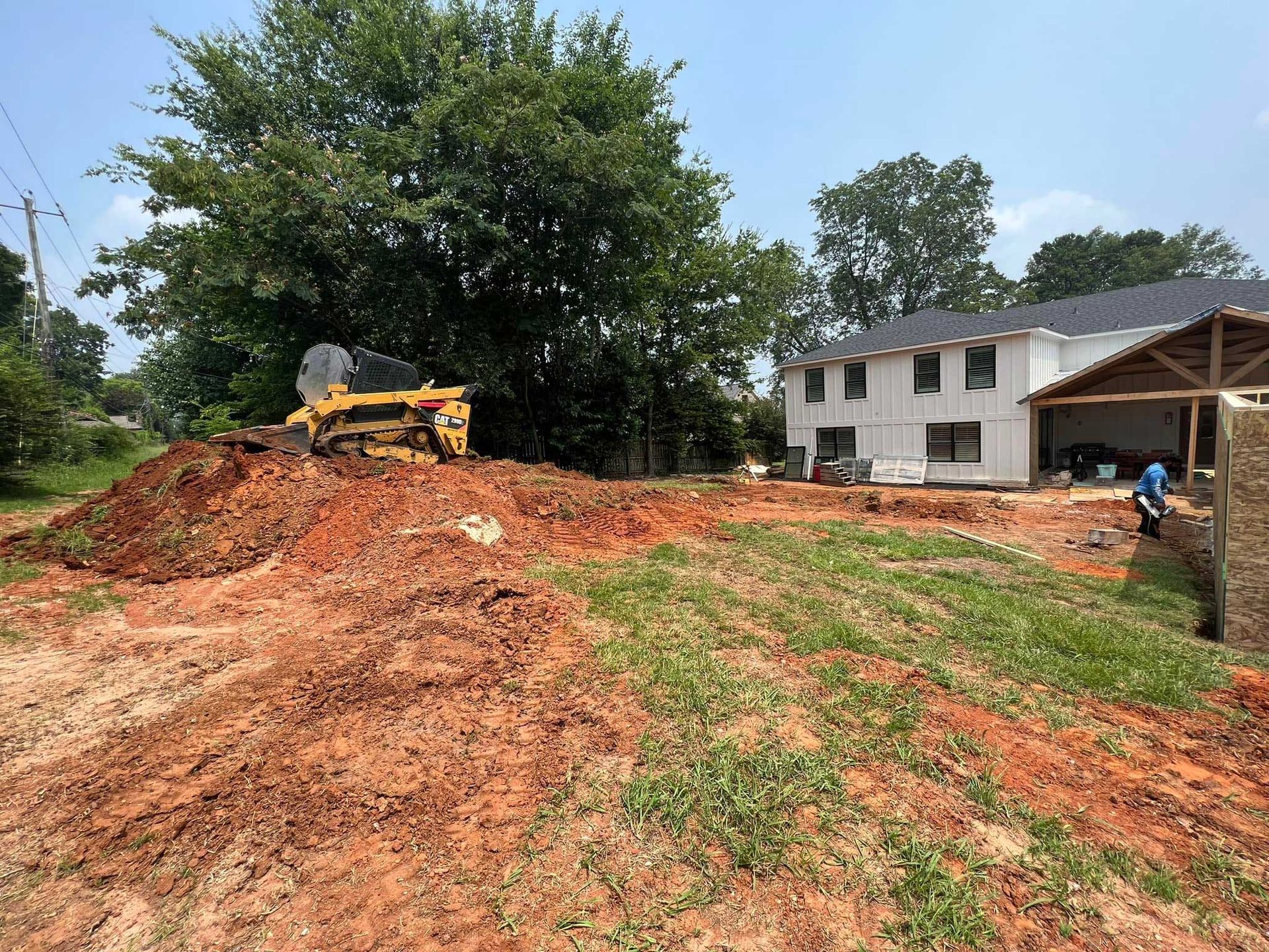 Construction site with a bulldozer on a dirt hill, house in background, sunny day.