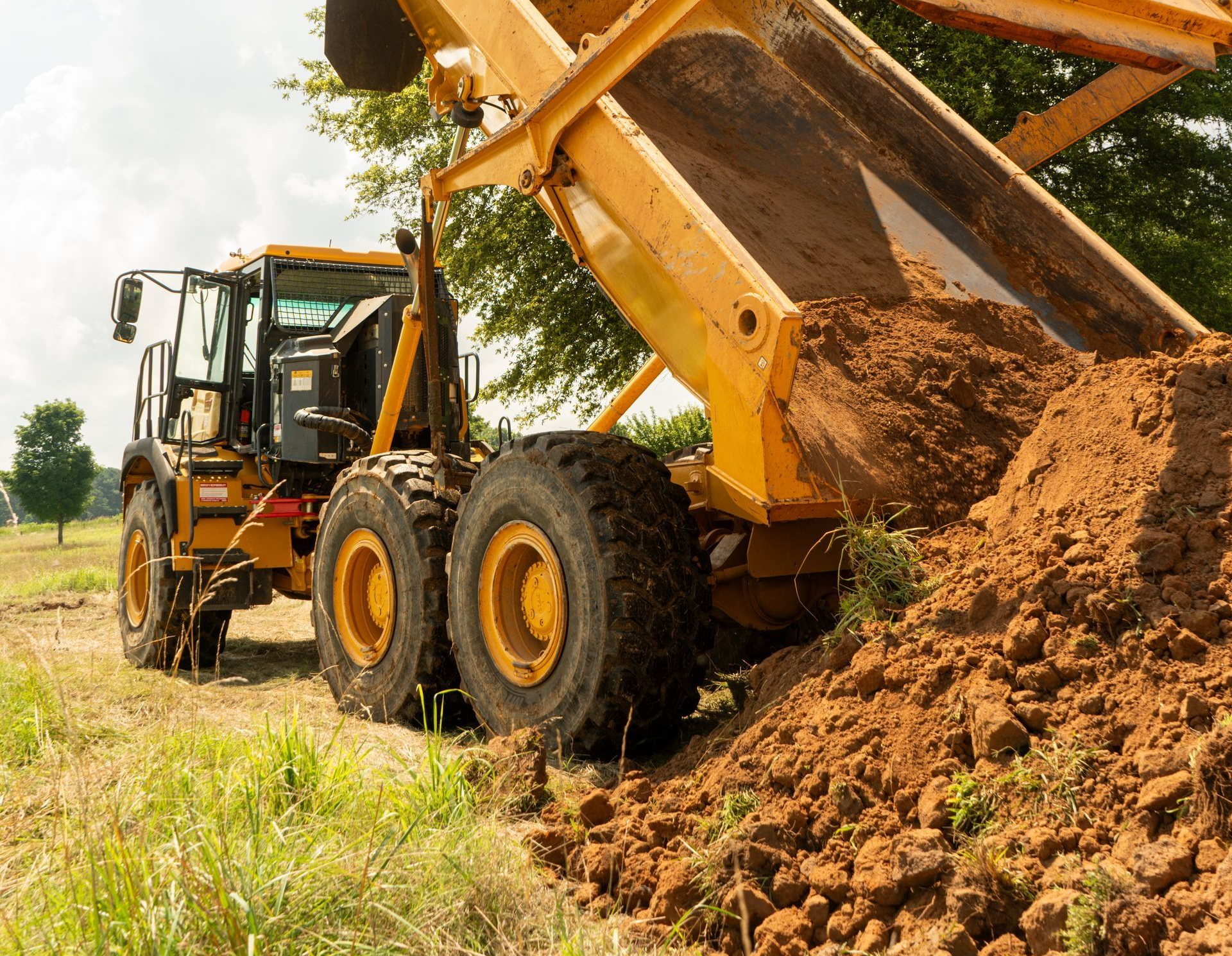 A yellow articulated dump truck unloading a large pile of dirt onto a field.