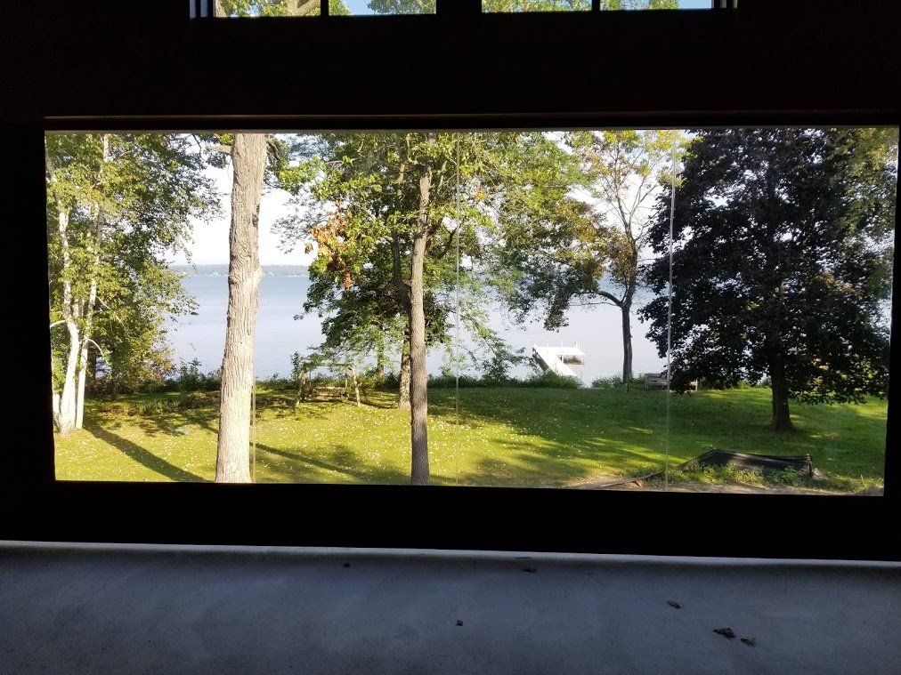 View of a lake and trees through a dark window. Green grass and foliage with blue water in the distance.
