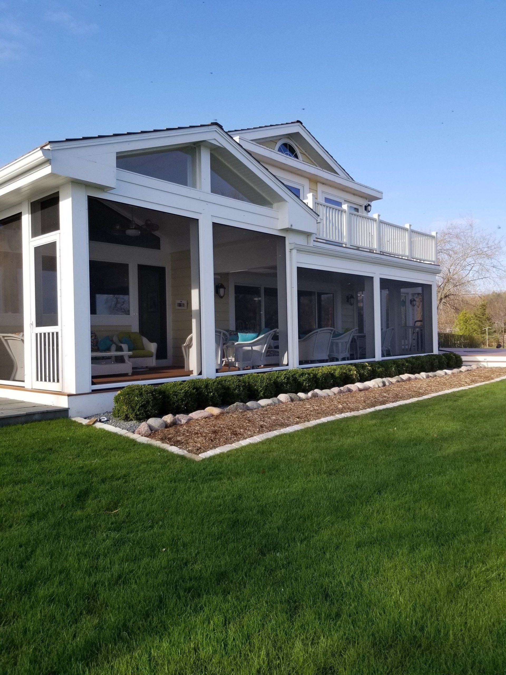Screened porch of a house with white pillars, overlooking a grassy lawn and a clear blue sky.