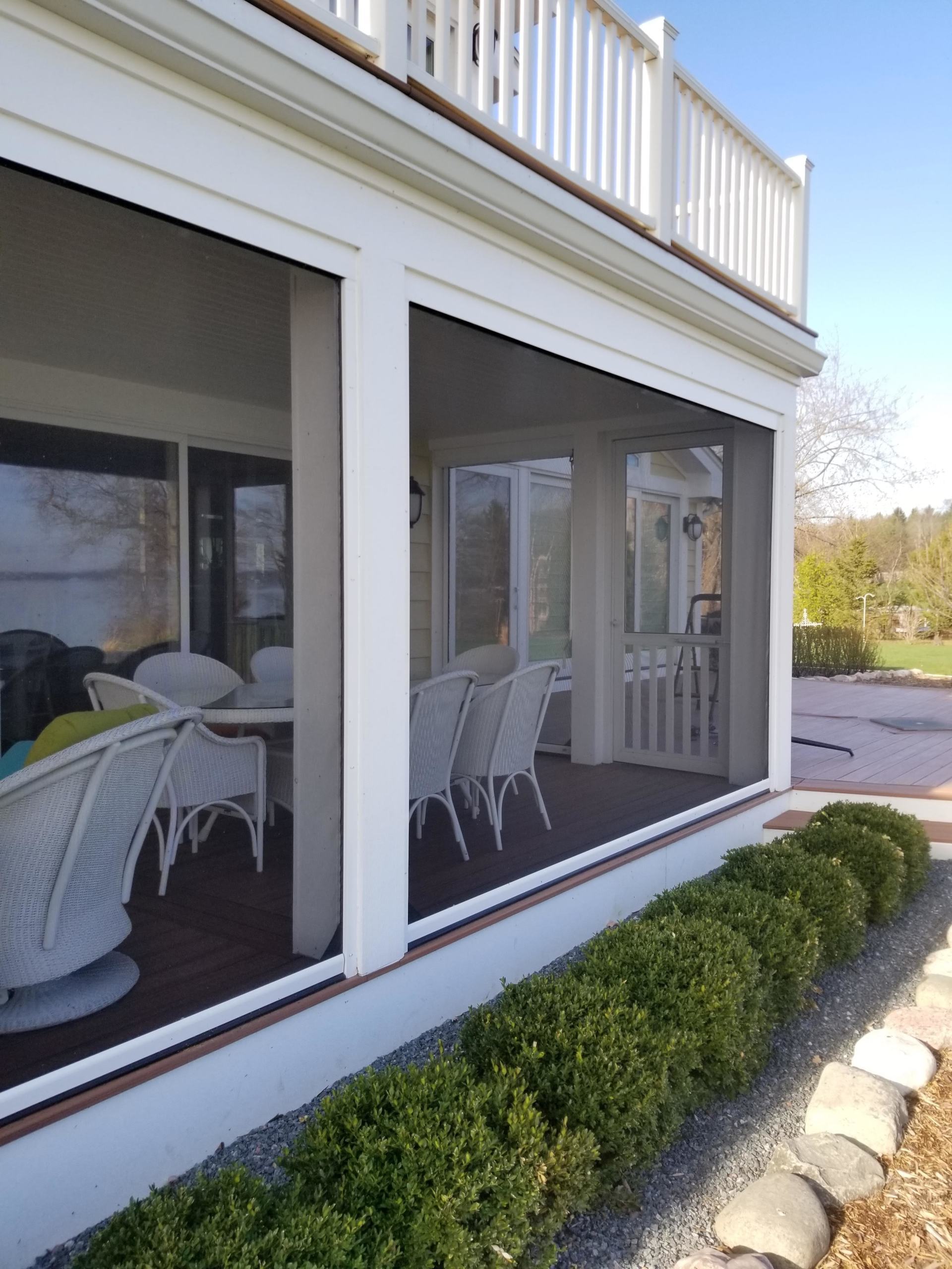 Screened-in porch with white columns and railings. Chairs and a table are inside. Bushes line the exterior.