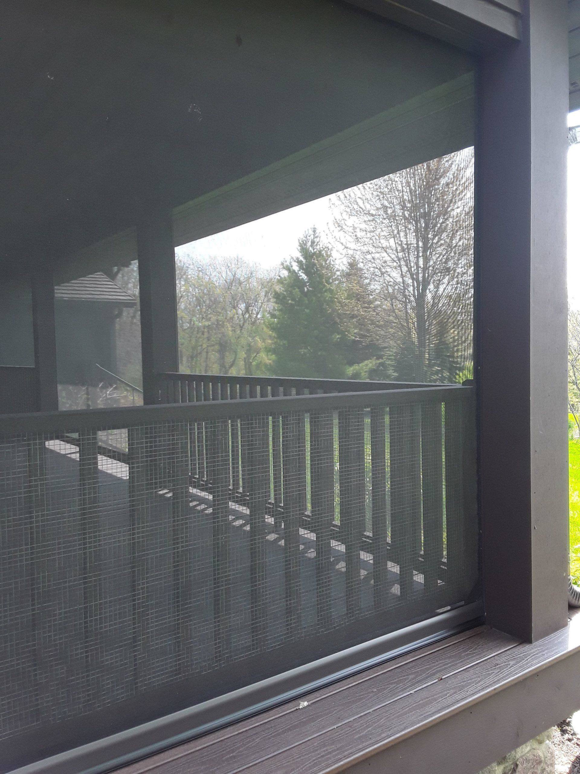 Outdoor deck with a retractable screen. The dark screen is partially down, providing shade while allowing a view of trees and the surroundings.