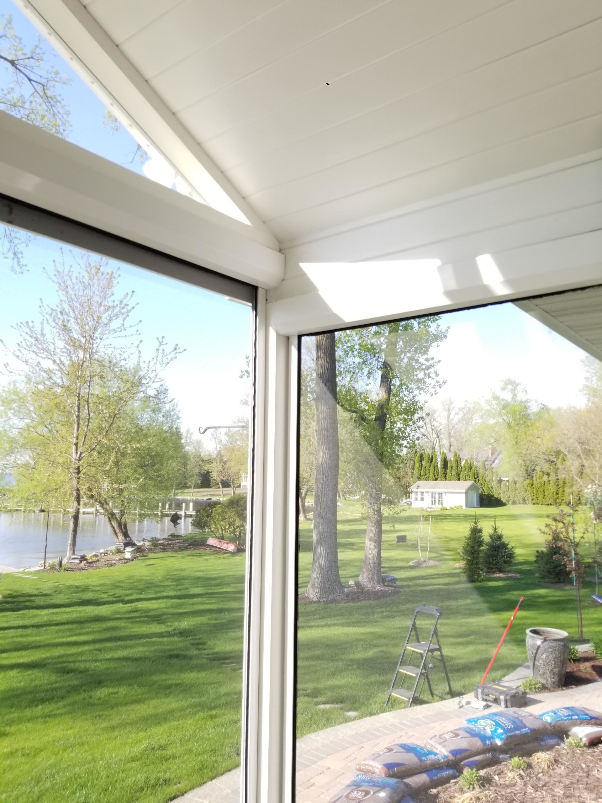 View from a white-framed screened porch overlooking a lake and grassy yard. Green trees and blue sky visible.