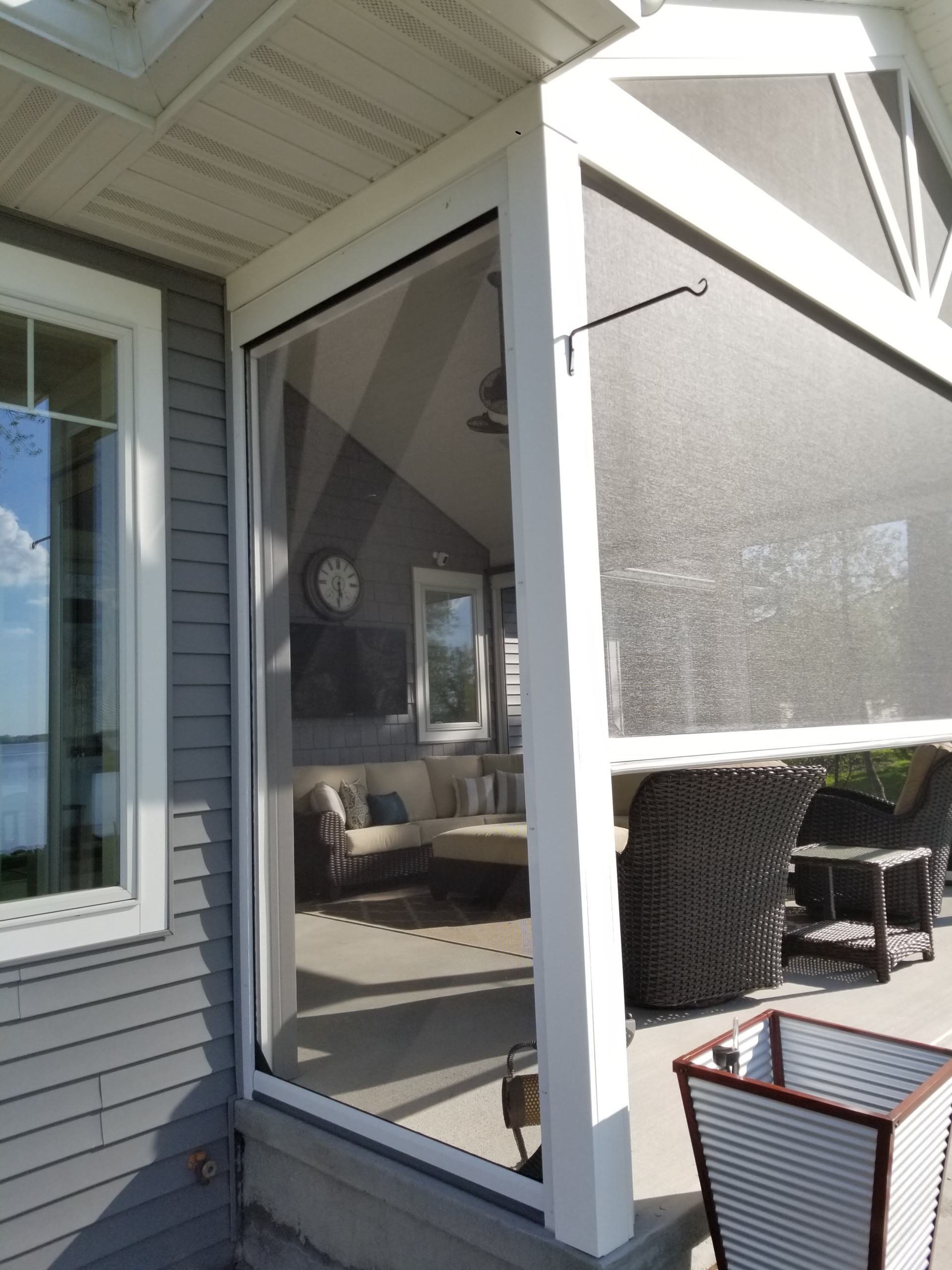 Exterior view of a screened porch with a retractable screen and outdoor furniture. The house has gray siding and white trim.