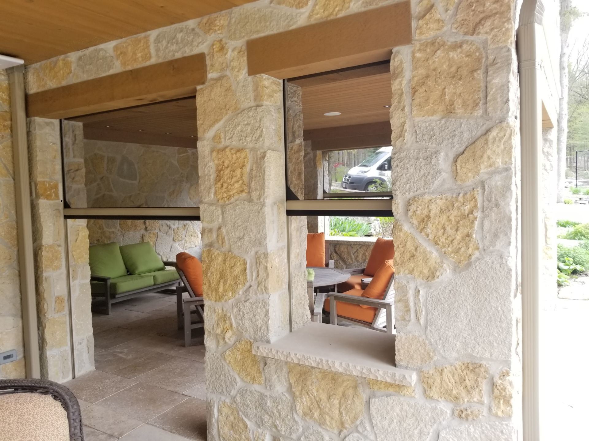 Stone-walled outdoor space with two open windows, featuring a seating area with green couch on the left and an outdoor dining set on the right.