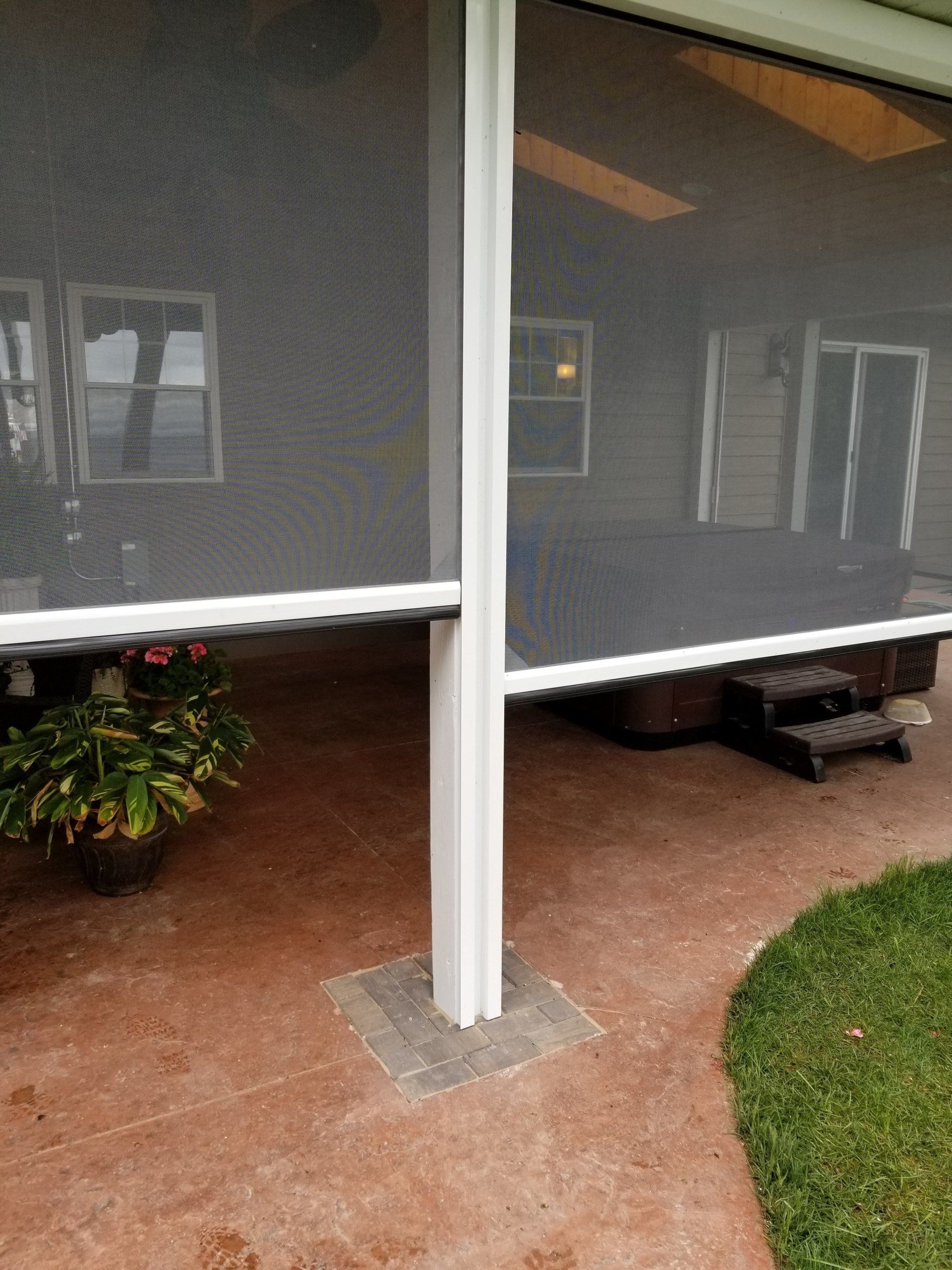 A patio with a retractable screen and a white support column. A hot tub is visible in the background.