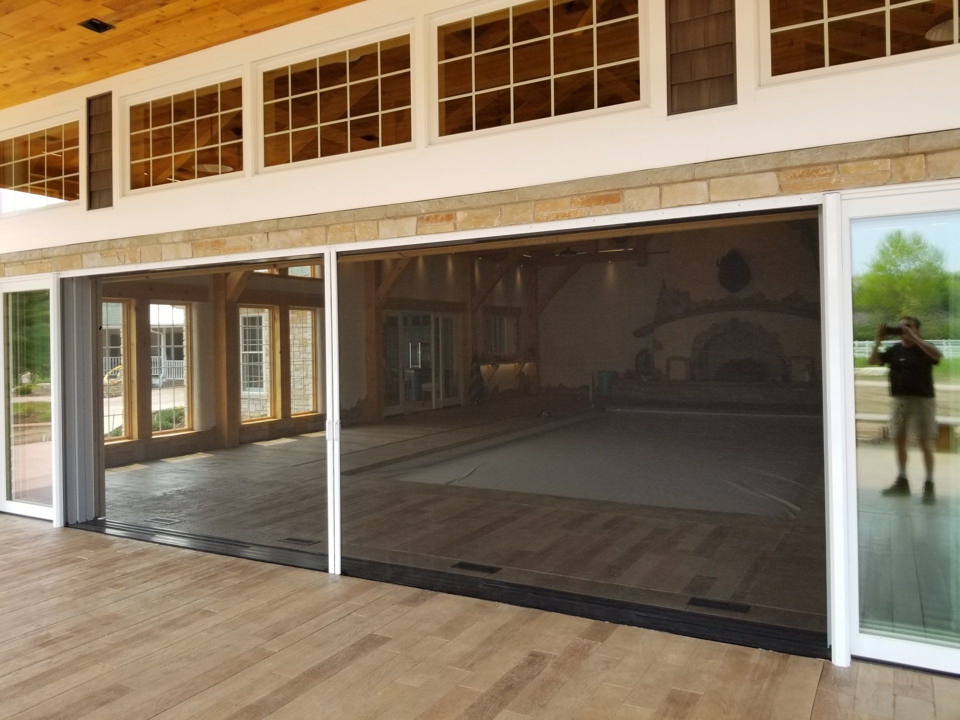Large retractable screen door on a deck, revealing an interior with wooden floors and a light-filled space.