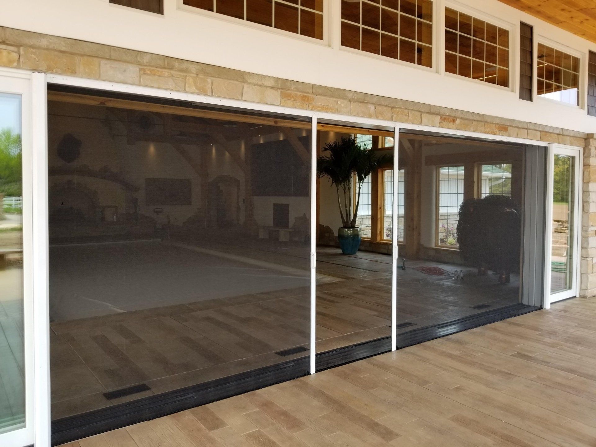 A set of large, retractable screen doors on a patio, partially open, allowing a view into a home with a pool.