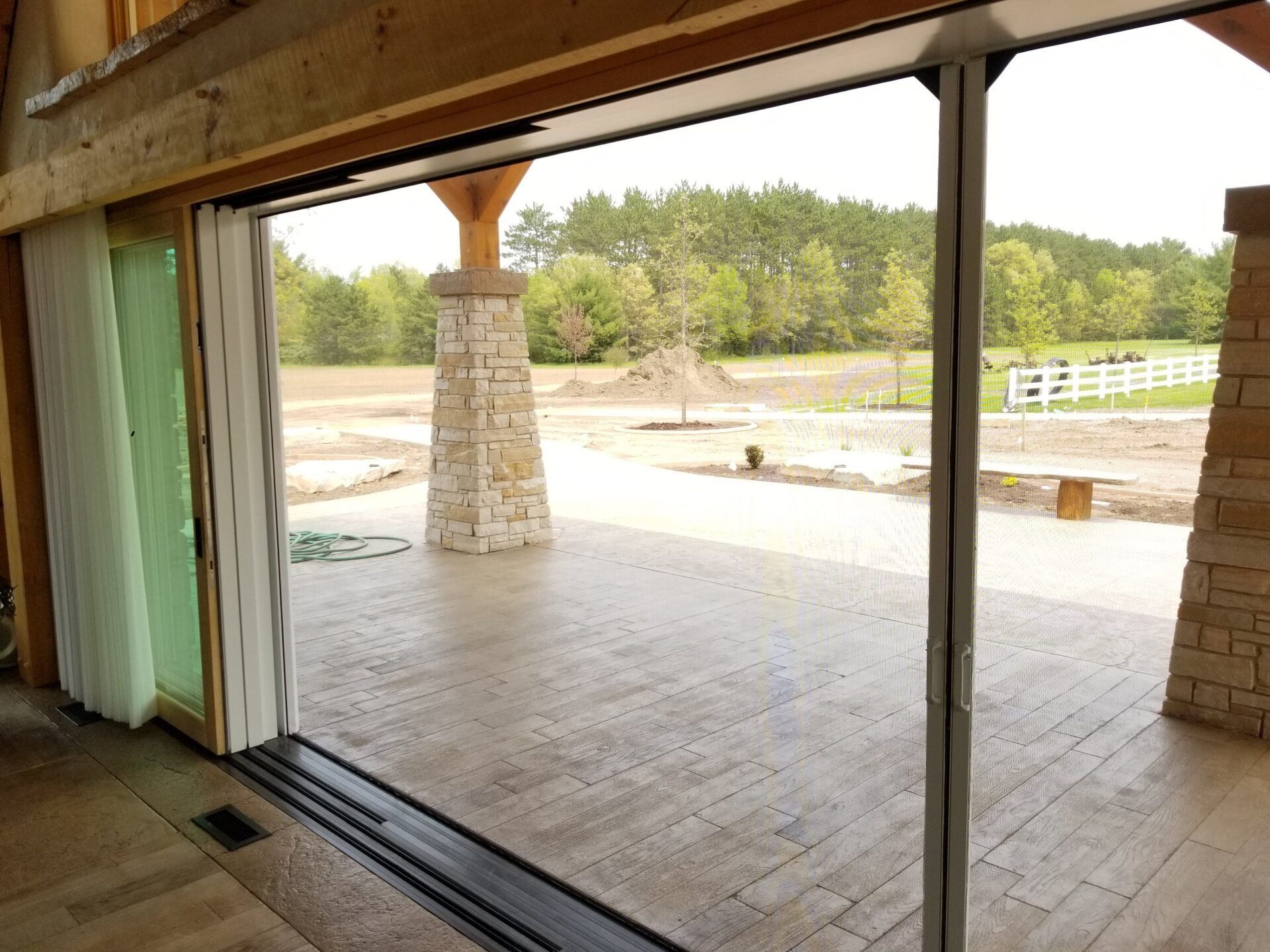 Open sliding glass doors reveal an outdoor patio with stone pillars and a view of trees and a fence.