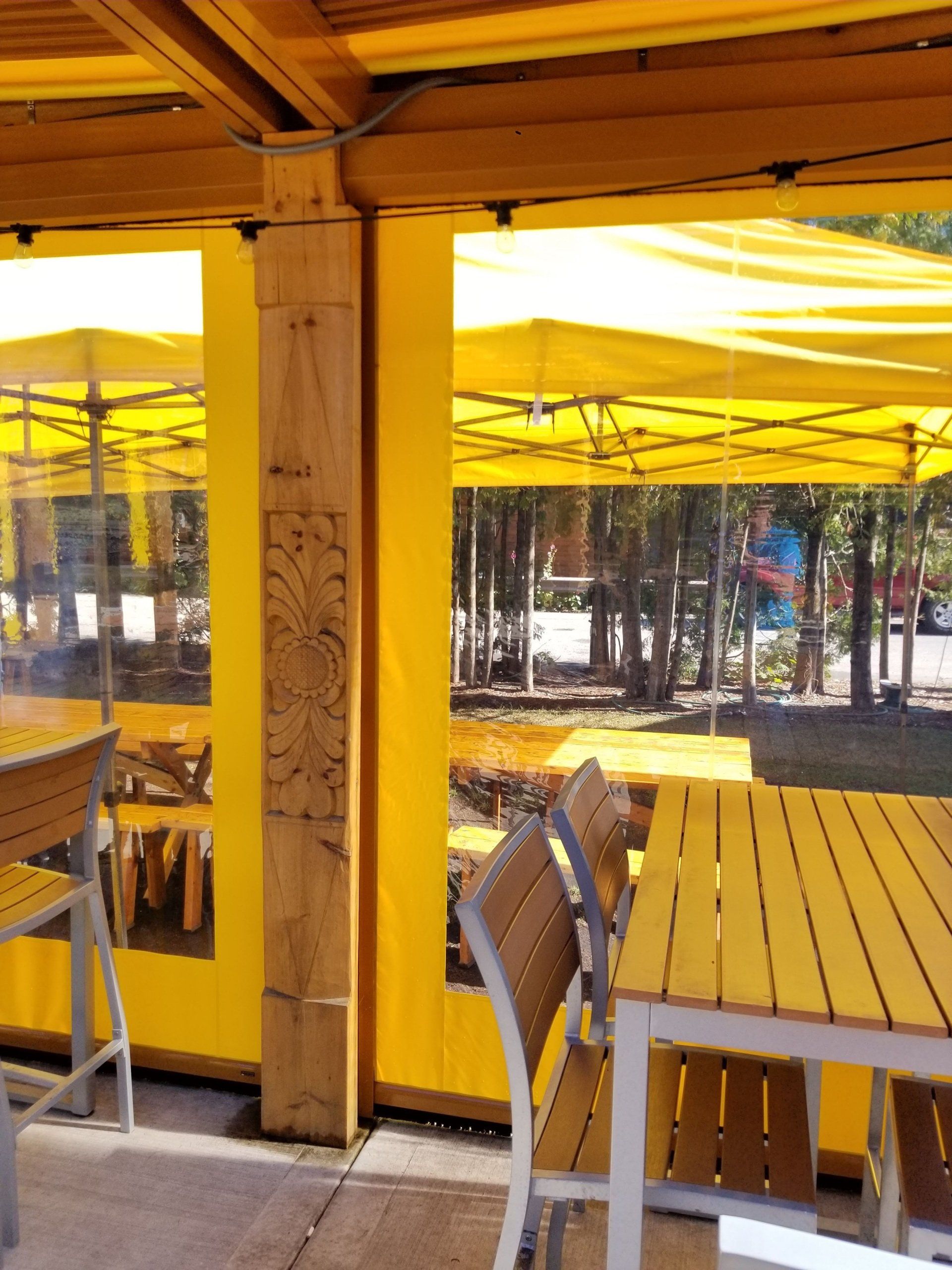 Outdoor dining area with yellow awnings, tables, and chairs. A wooden pillar with decorative carvings is visible.