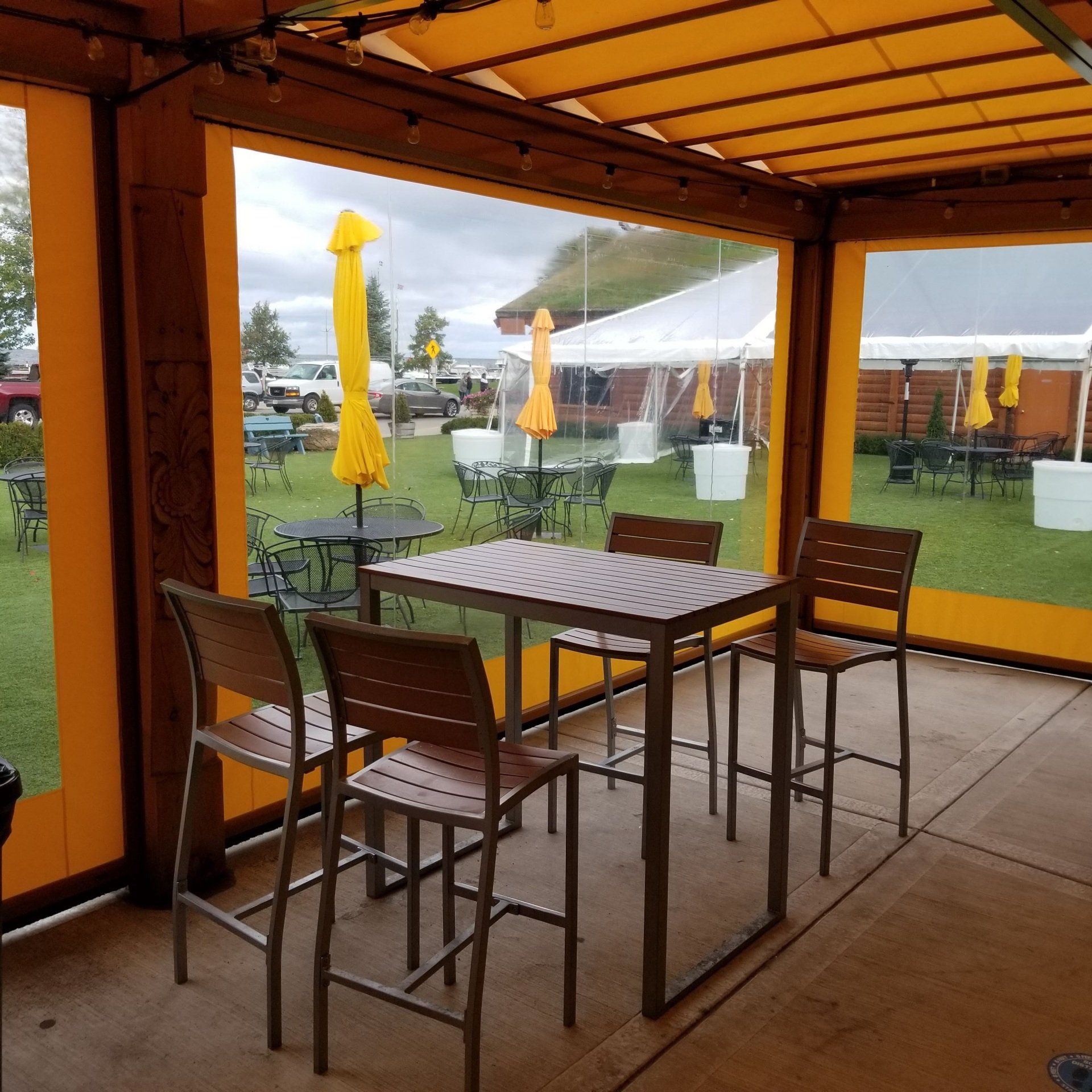 Outdoor dining area with a table and chairs inside a covered patio. Yellow awning and clear plastic walls.
