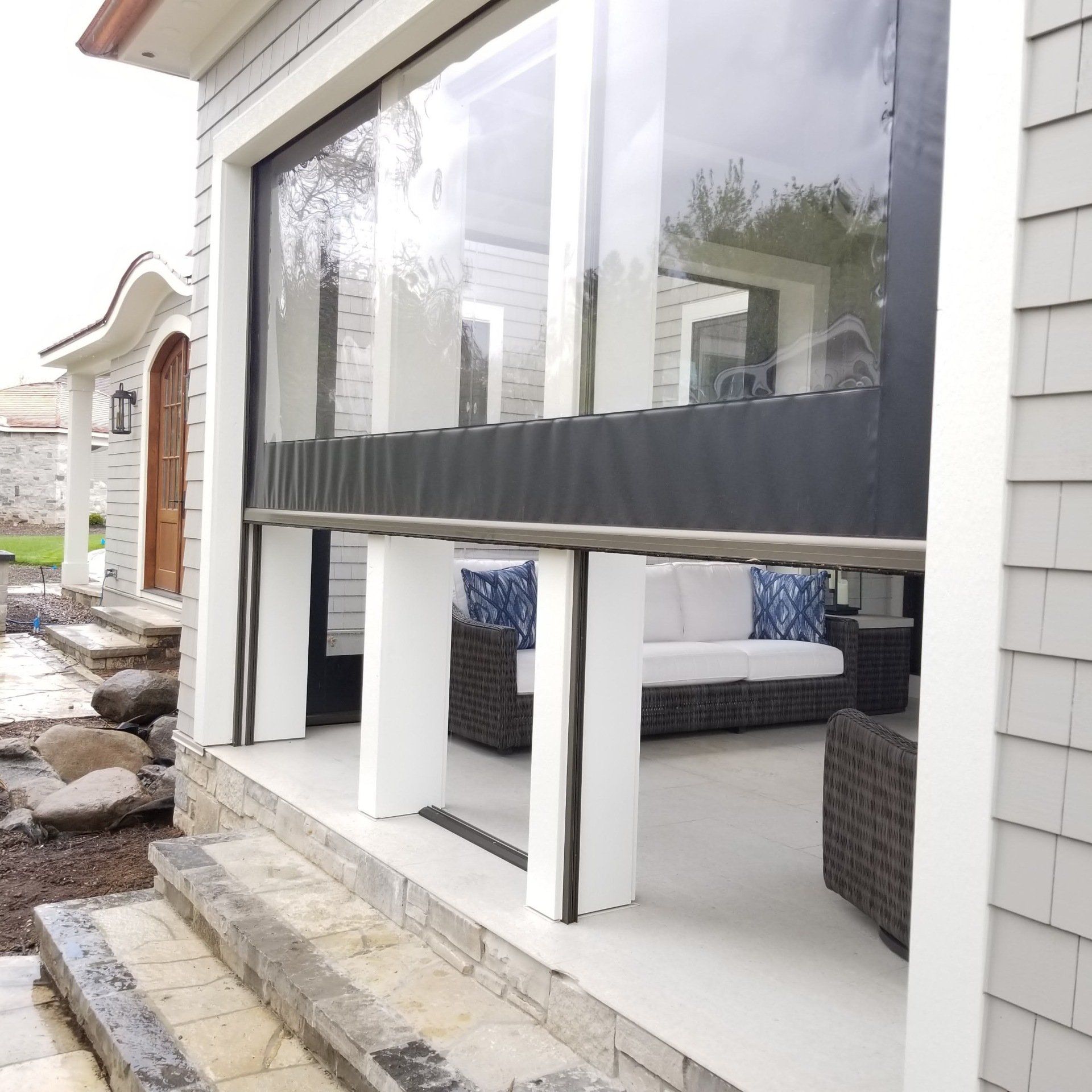 Outdoor patio enclosed with clear vinyl curtains, a white sofa and chairs are inside.