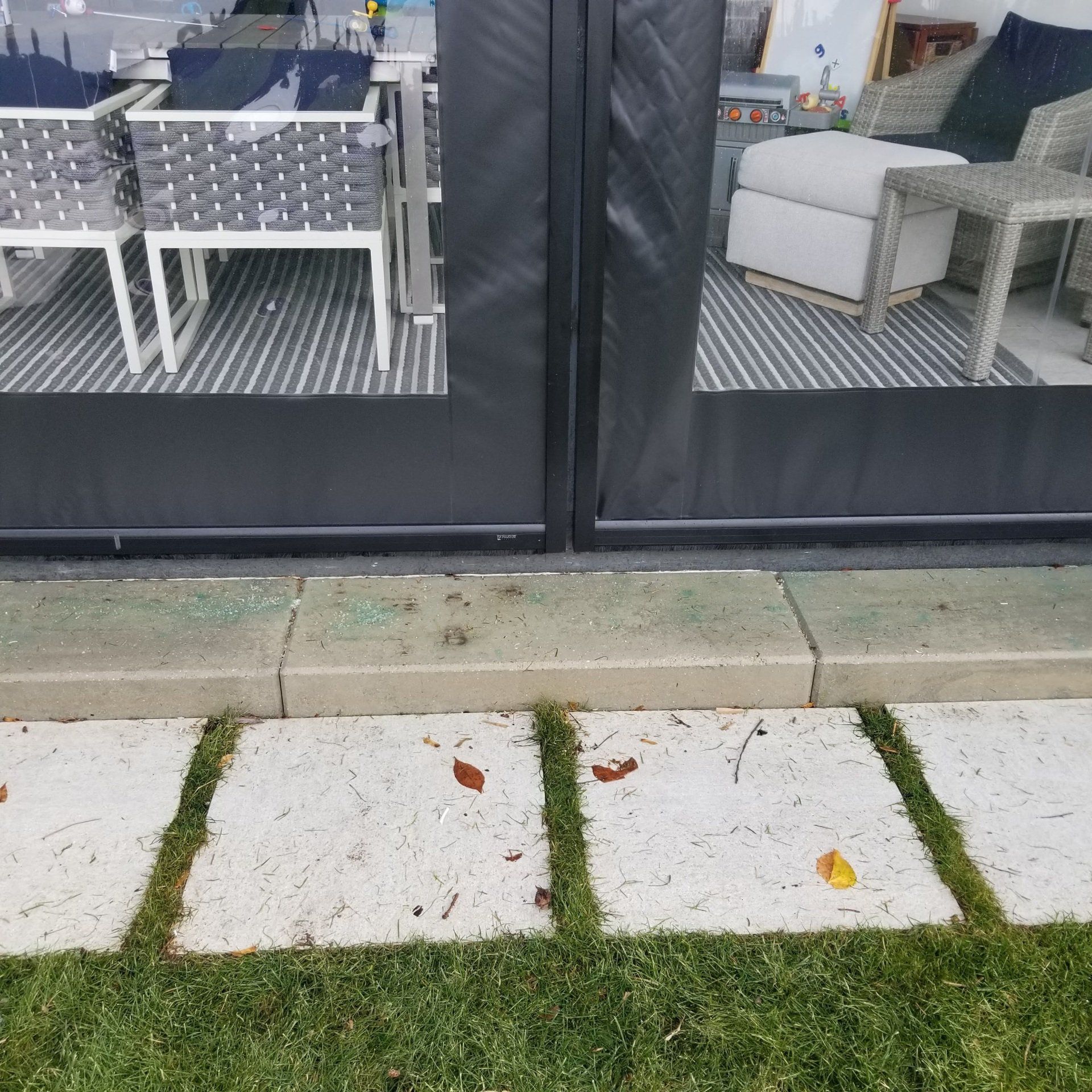 View of a patio door with outdoor furniture visible through the glass. Stepping stones and grass are in the foreground.