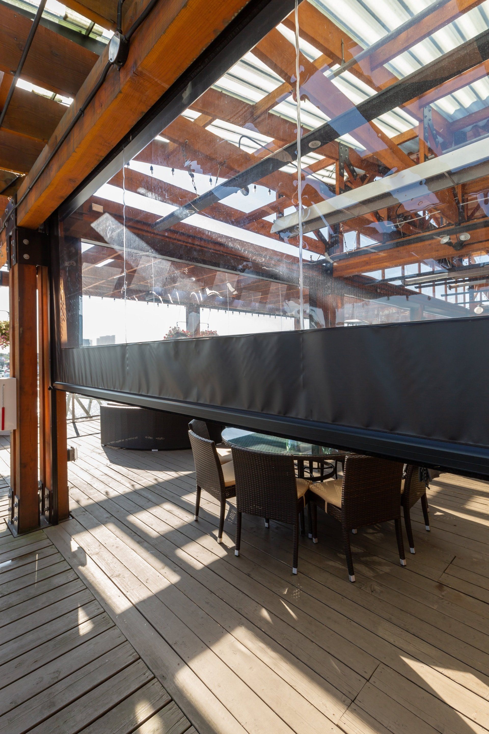 Outdoor patio with a dark awning, table, and chairs under a clear roof. Wooden deck and beams.