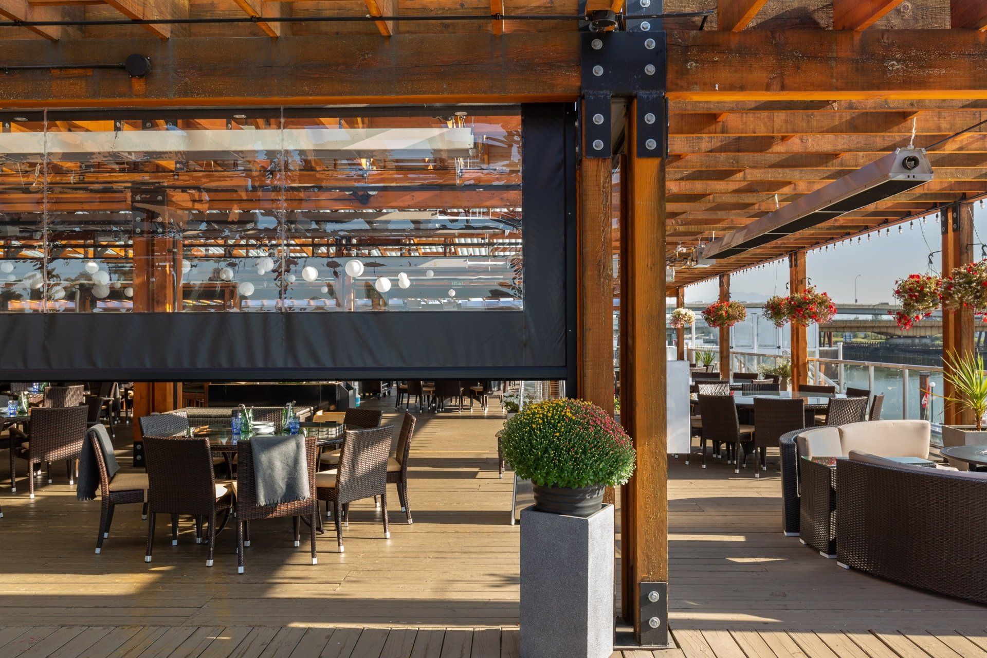 Outdoor restaurant patio with wooden pergola, tables, and chairs. A retractable screen and heaters are visible.