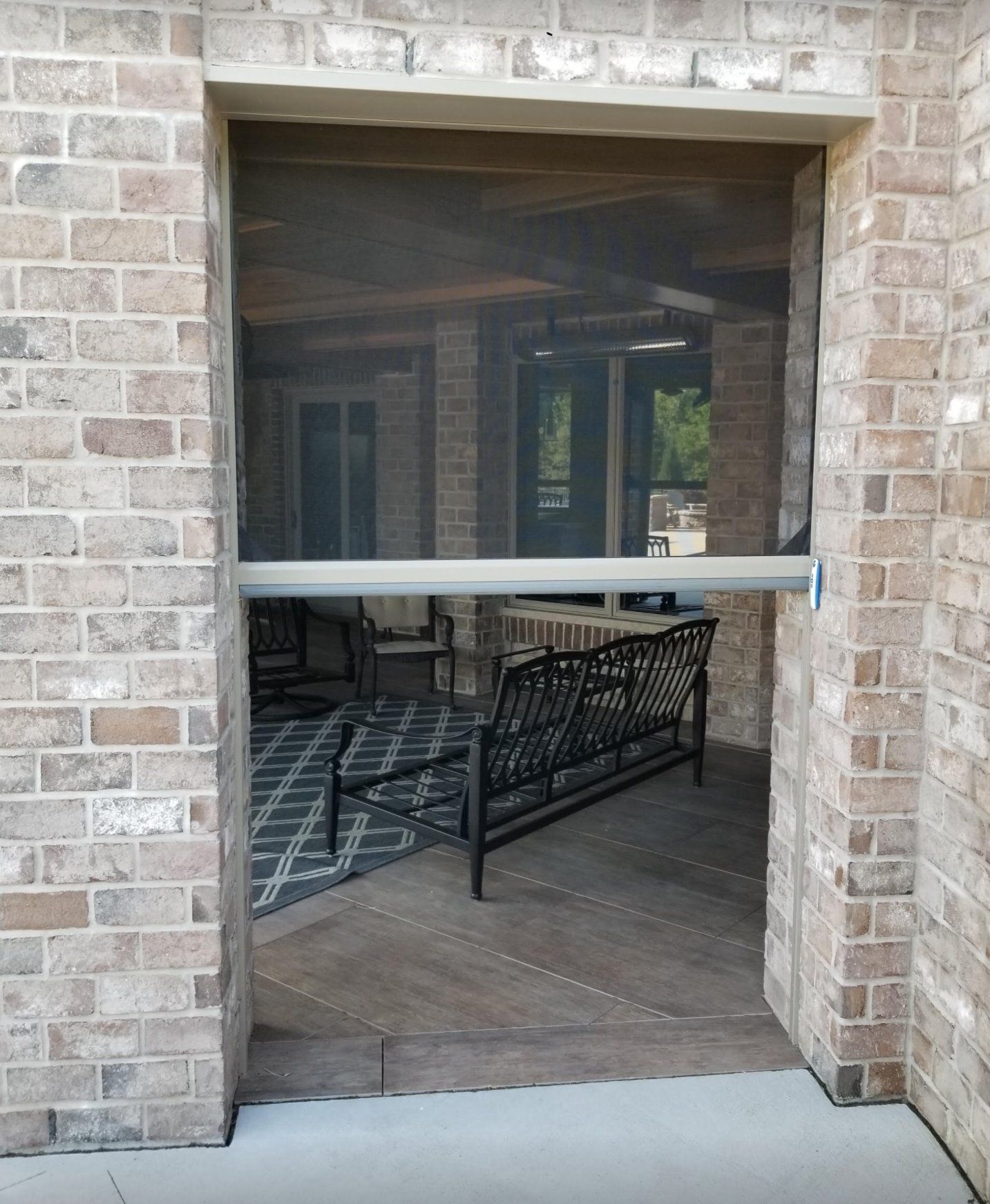 Screened doorway opening to a covered patio with brick exterior. A gray screen is partially lowered.