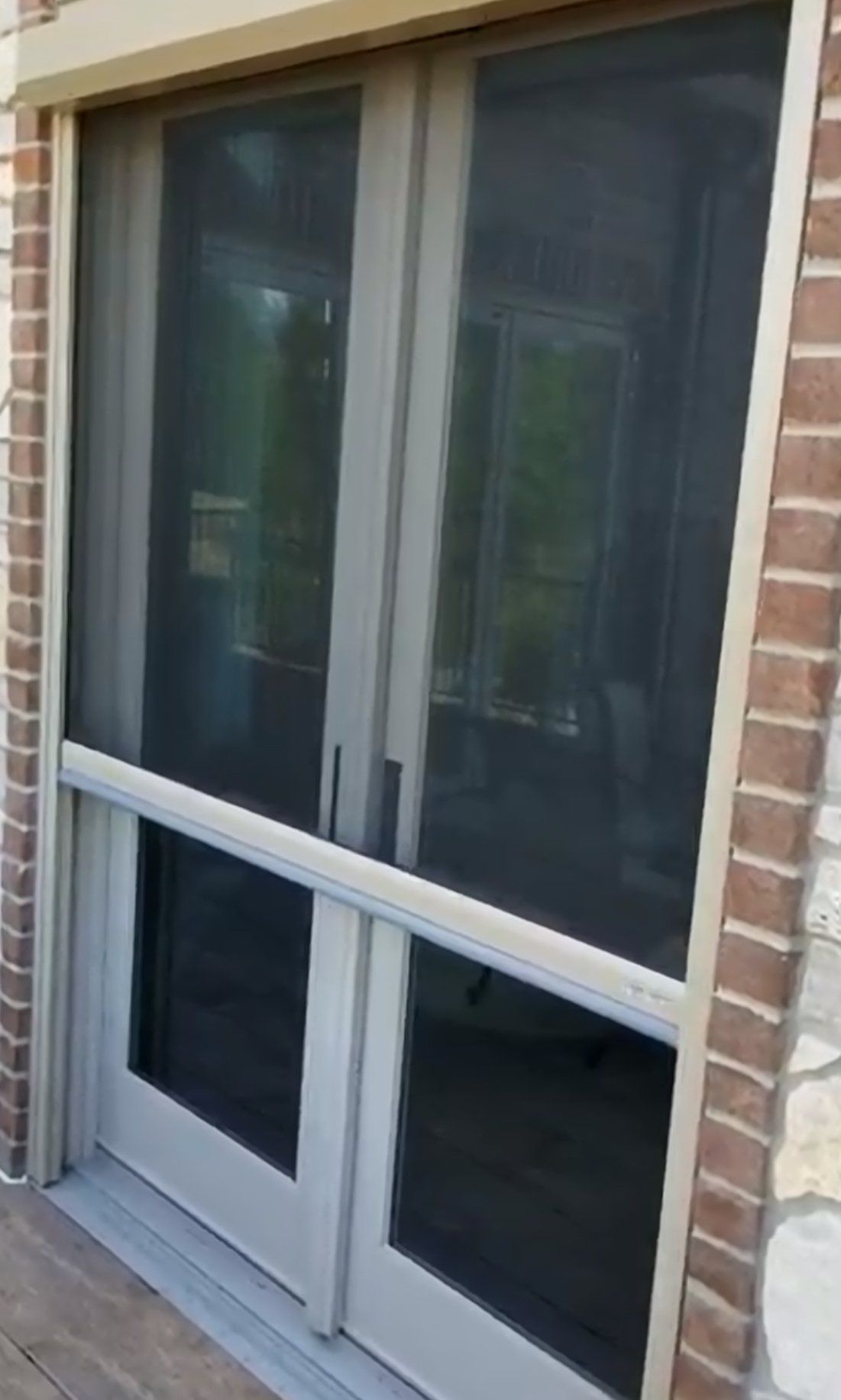 Screened French doors, beige frame, open to a porch or patio, seen from the outside. The doors are flanked by brick and stone.