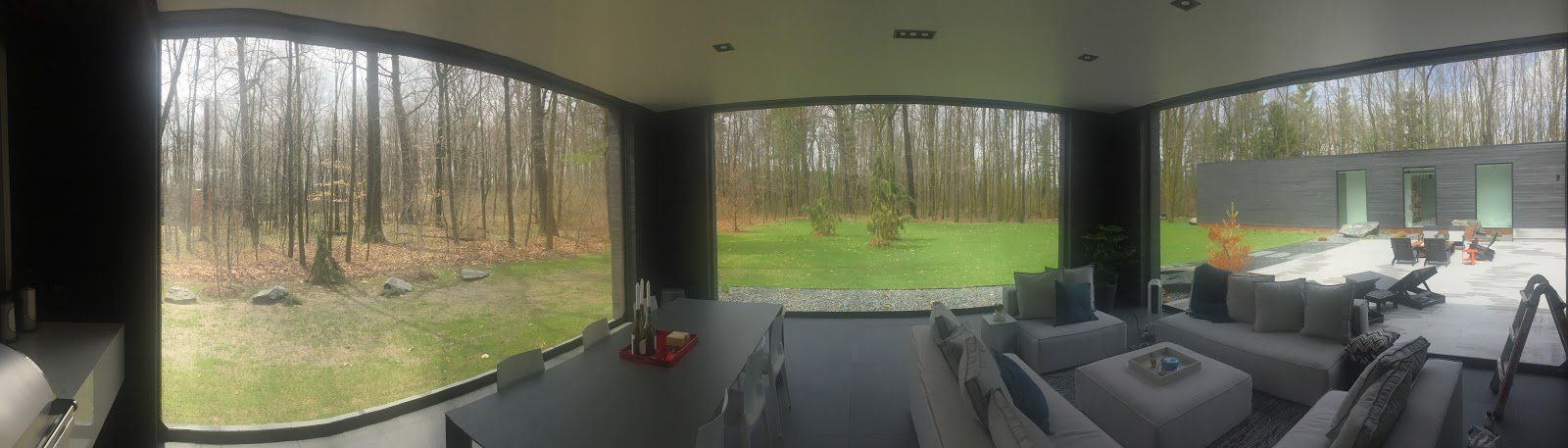 Modern interior with large windows overlooking a forest. Living room features a gray sofa, coffee table, and outdoor seating area.
