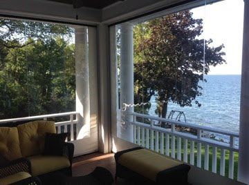 A screened porch with a view of a lake and trees. Comfortable seating is visible.
