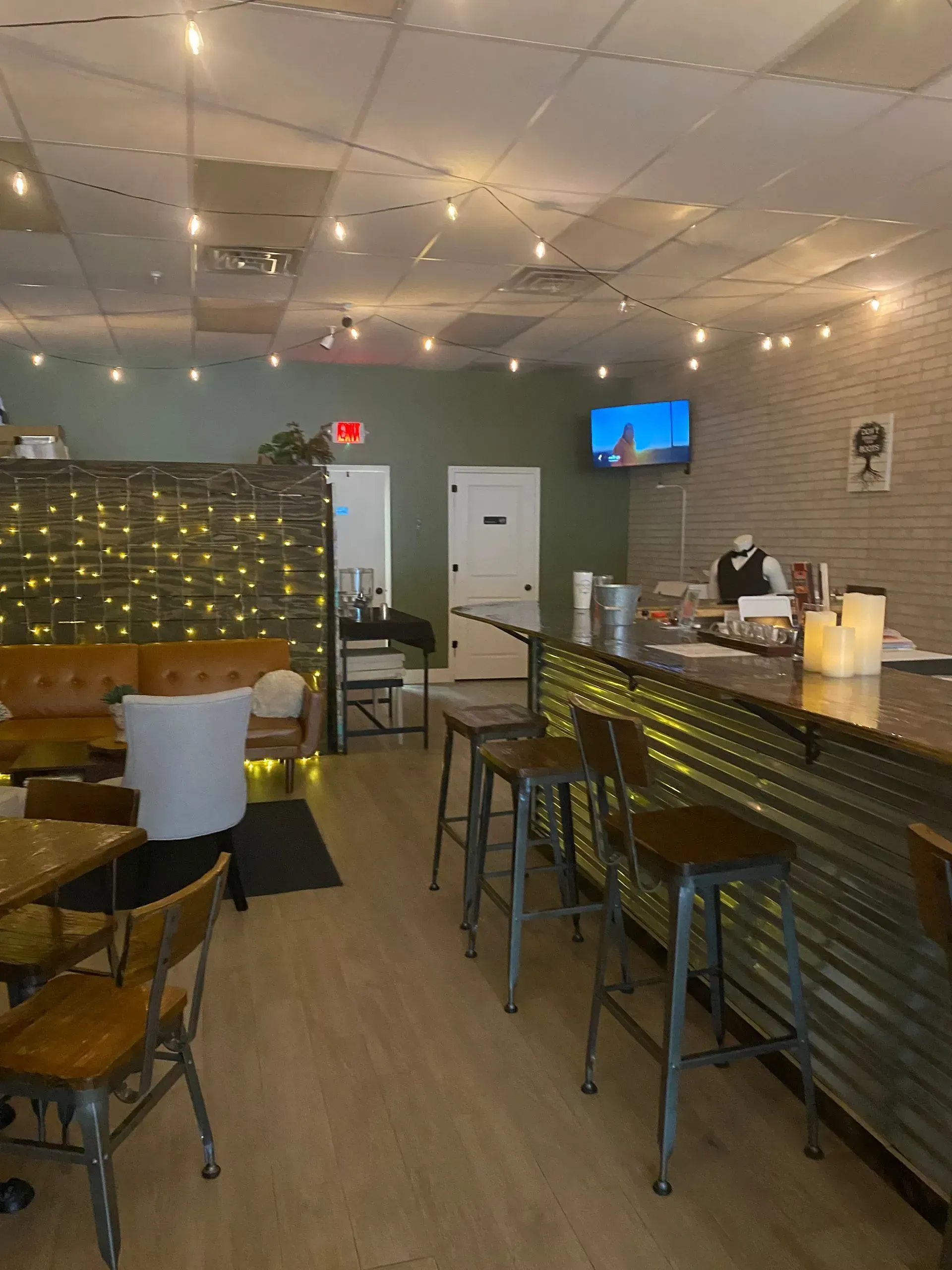 Restaurant interior: bar with stools, tables, and a lounge area with string lights and brick wall.